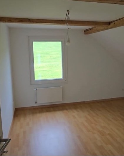 Empty room with a window, wooden beams on the ceiling, and hardwood flooring.