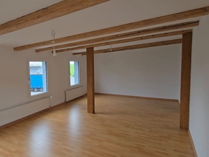 Empty room with wooden beams on the ceiling, white walls, hardwood floor, two small windows, and a radiator.
