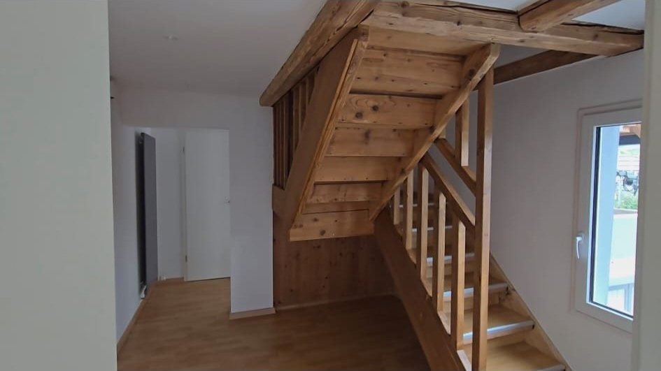 Wooden staircase leading to an upper level in a room with white walls and a window.