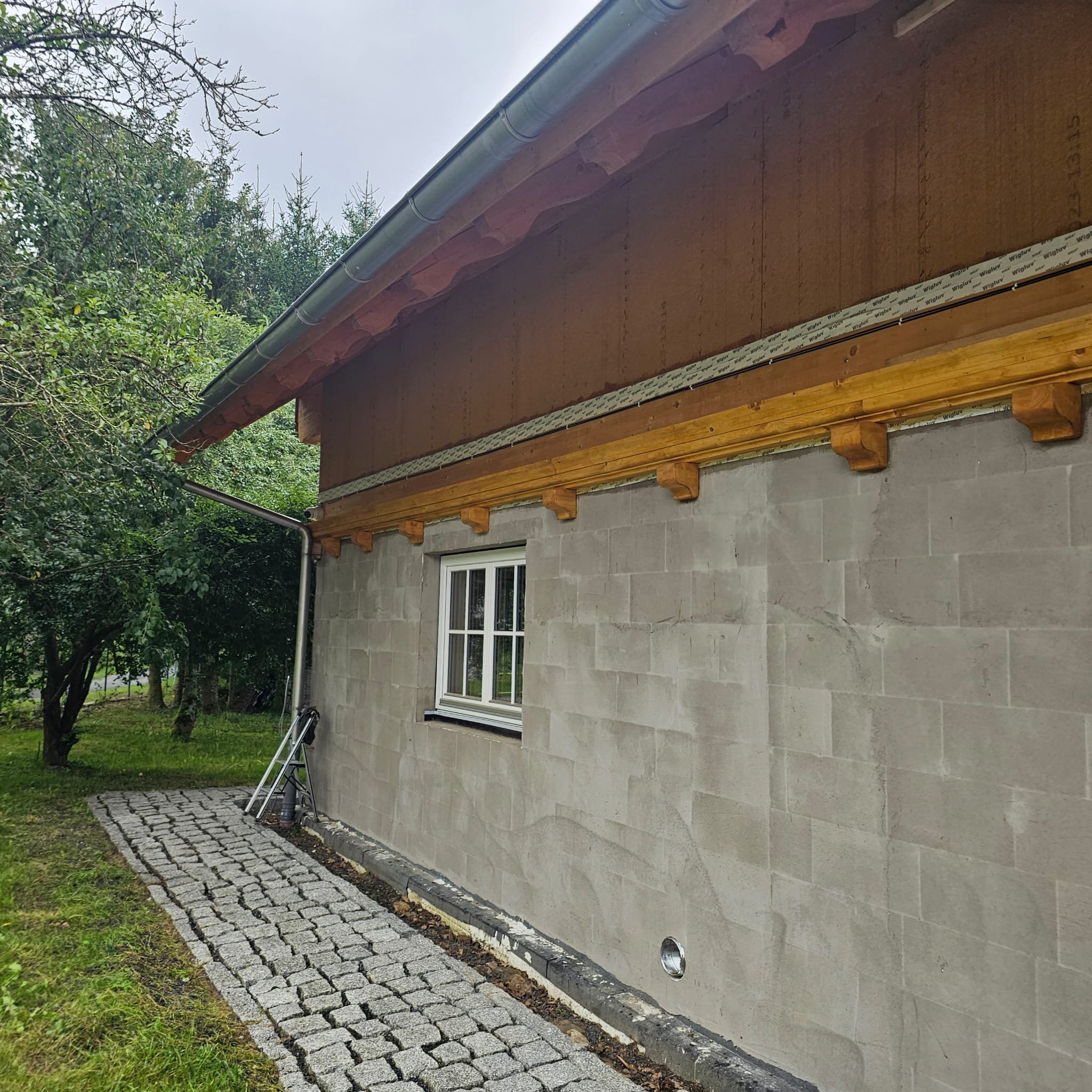 Side view of a building under construction showing a concrete block wall with a window, wooden beams, and acid rain signs on the roof.