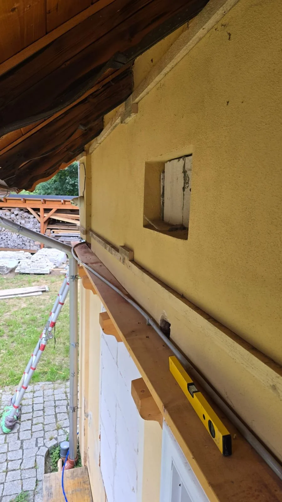 Construction site with yellow stucco wall, window opening, wooden beams, and construction tools.