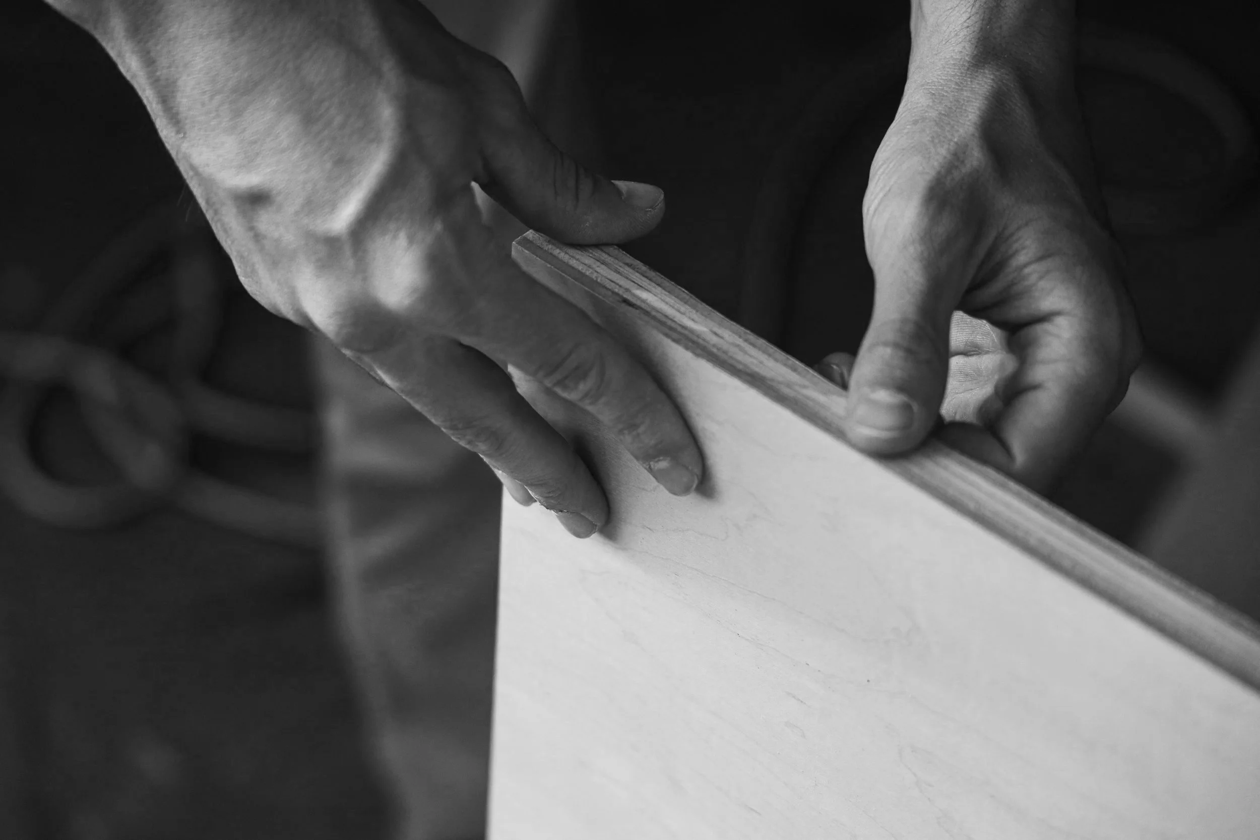 Close-up of a person's hands holding a piece of wood, appearing to sand or smooth the edge.