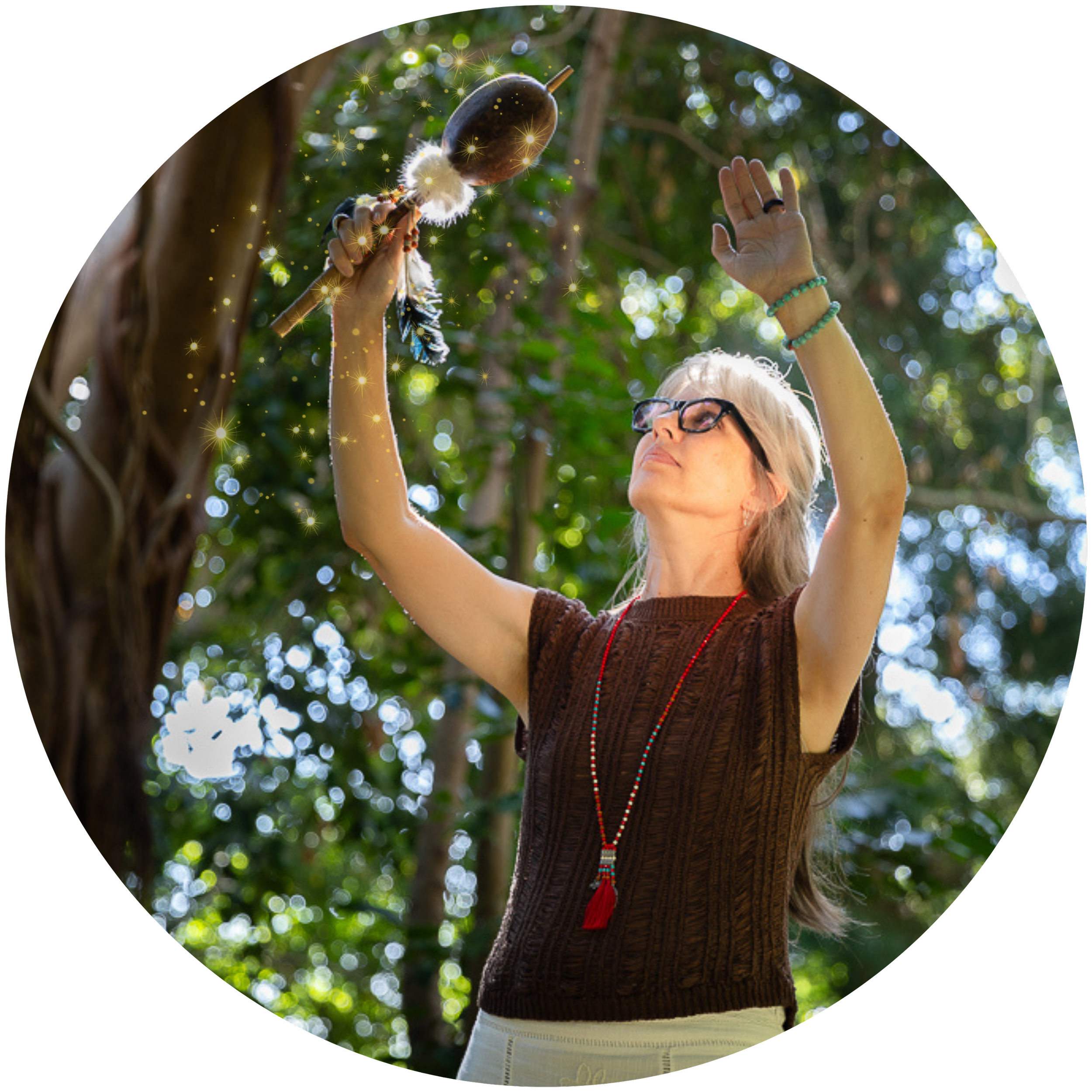 Alrina Laker raising a shamanic rattle toward the sky in a forest, representing the energetic transmission of the Munay-Ki Rites
