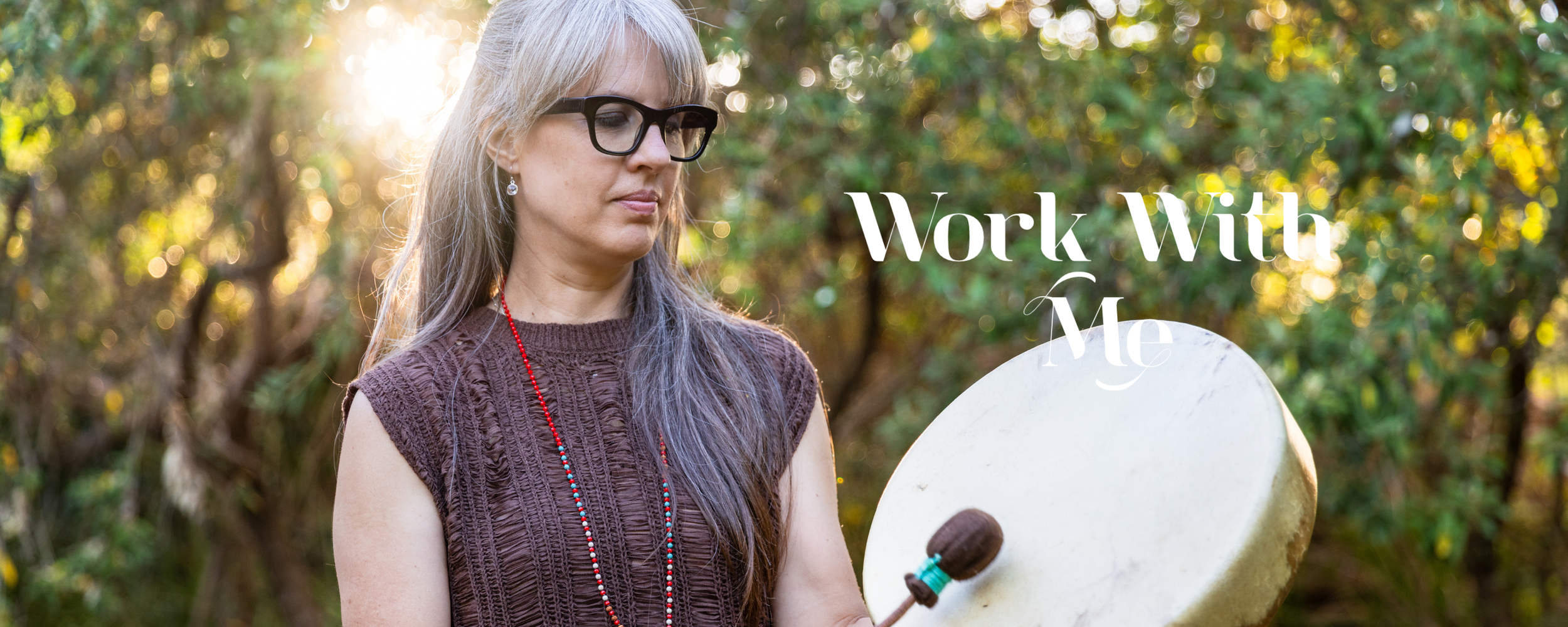 lrina Laker standing in a garden playing her shamanic drum, representing the 1:1 healing and transformation work offered at Sacred Ember
