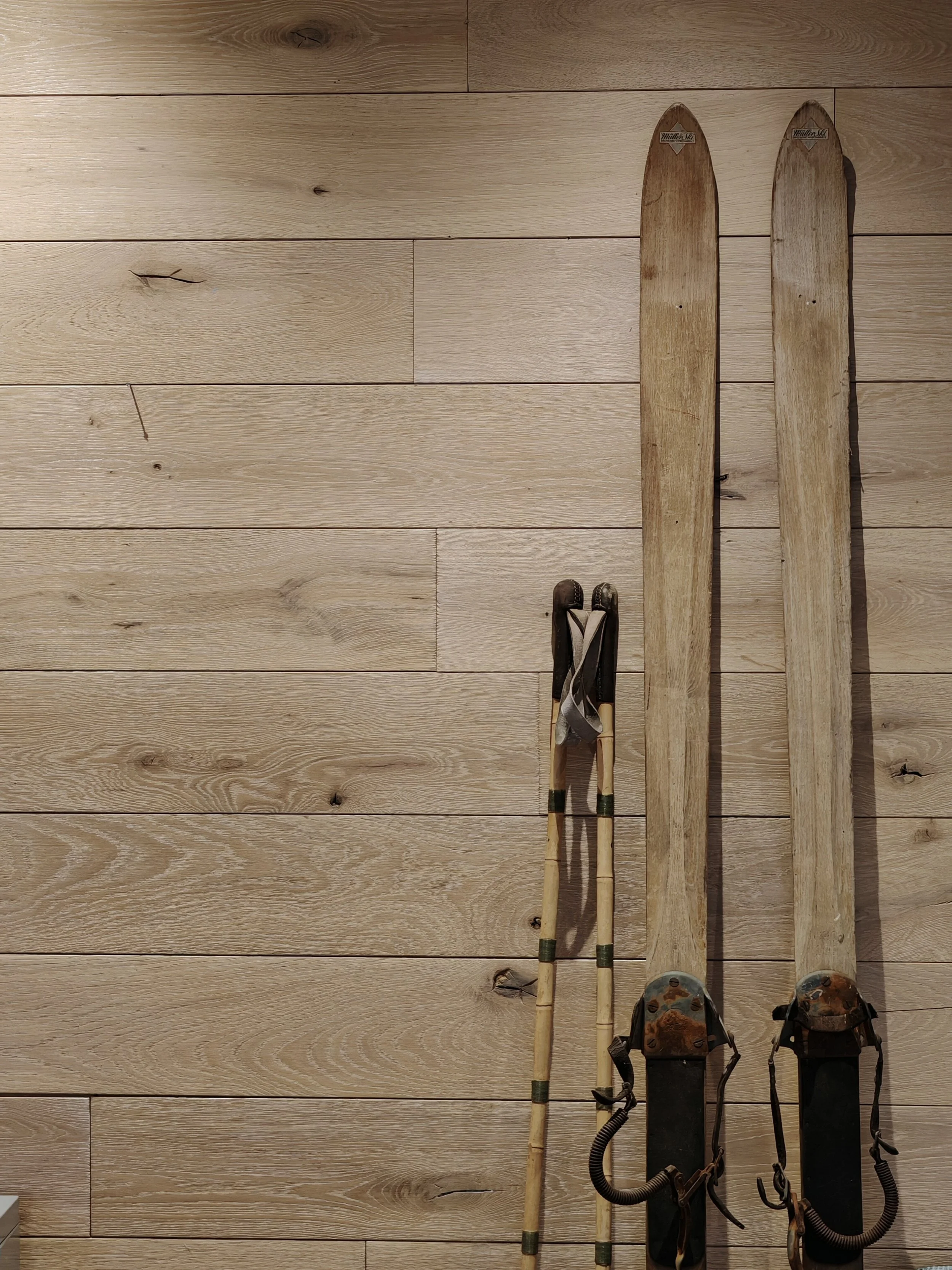 Deux skis en bois et un bâton de ski en bois reposent sur un sol en parquet Logic Nature en chêne massif 20mm d'épaisseur.