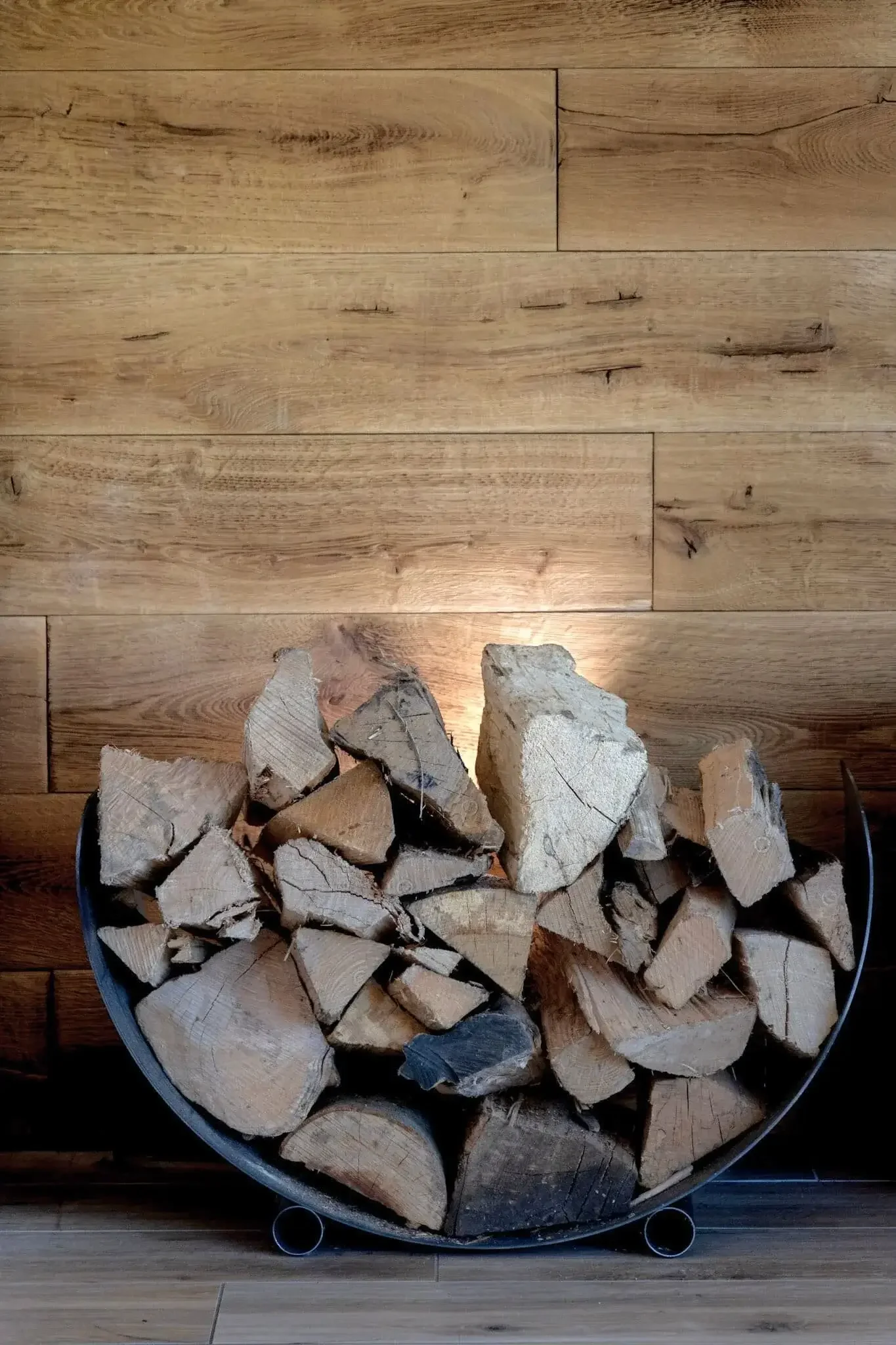 Bois de chauffage empilé dans un support en métal devant un mur en bois.