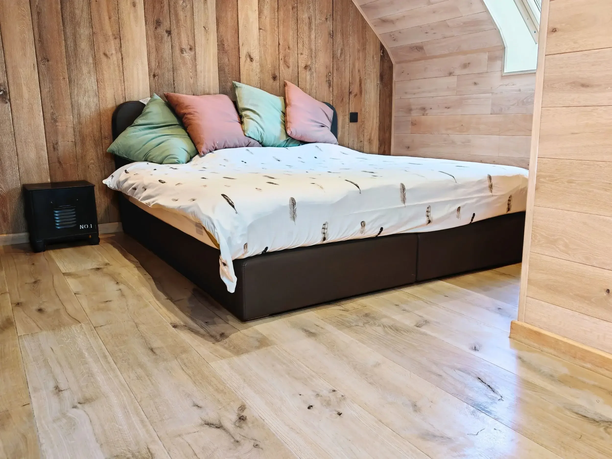 Lit double avec plusieurs oreillers colorés dans une chambre en bois.