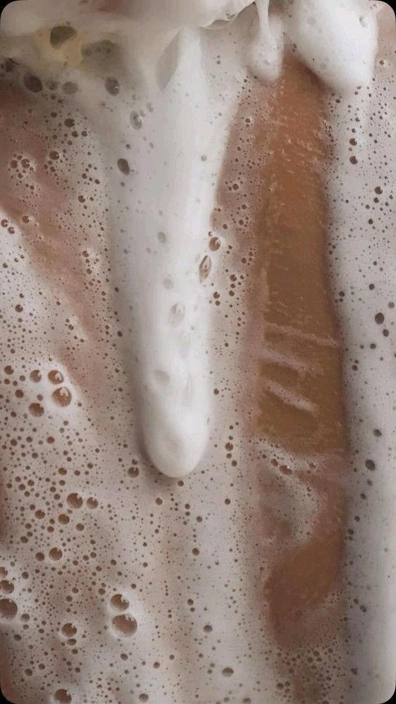 Close-up of a bar of soap in a bubbly bath or sink filled with soapy water.