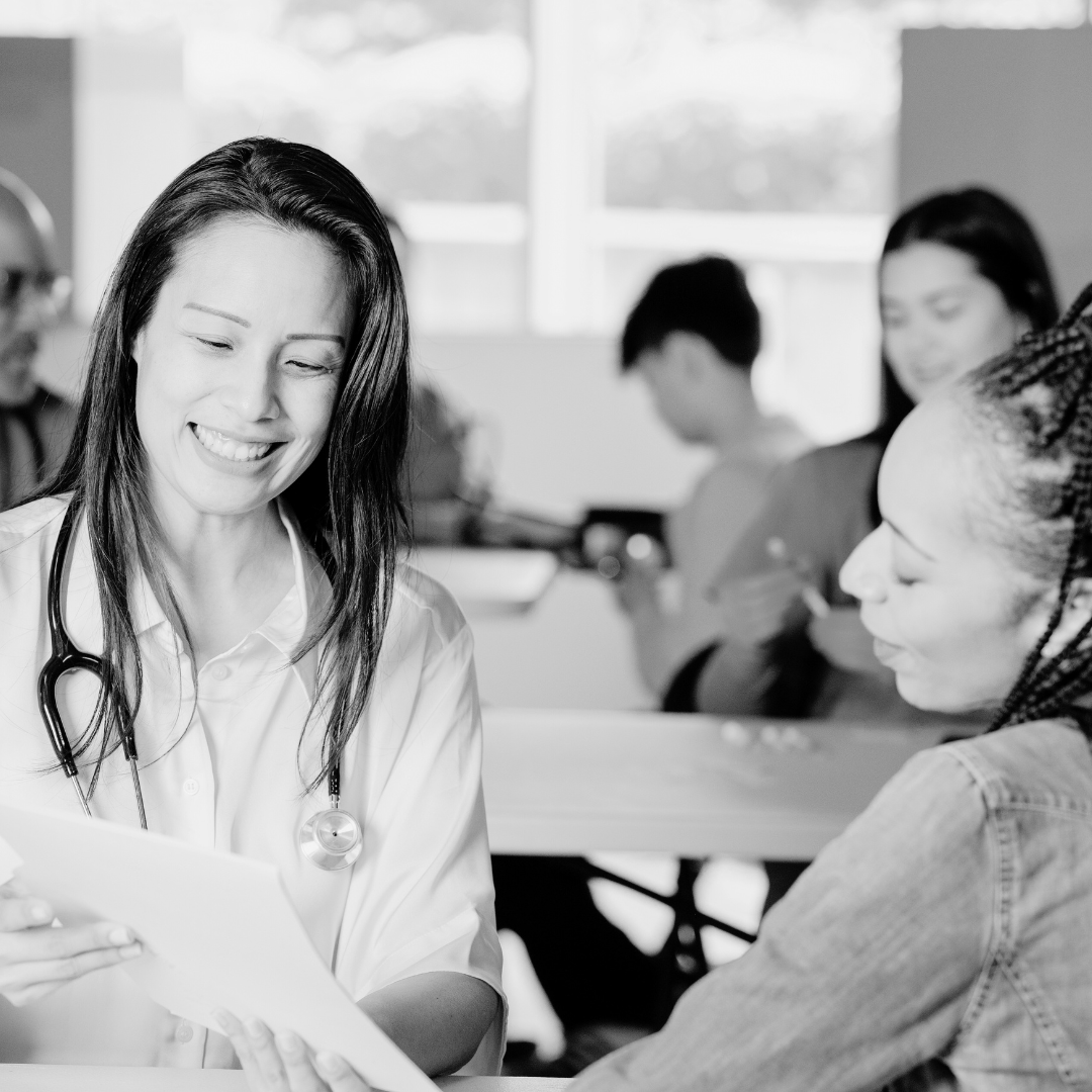 A female doctor with a stethoscope around her neck pointing to a piece of paper and showing another woman information in a clinic. 