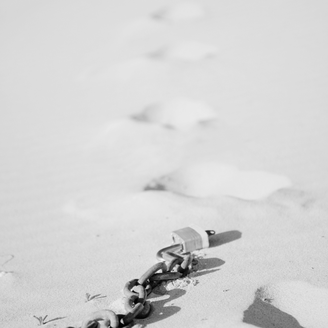 A broken chain laying in sand followed by footprints.