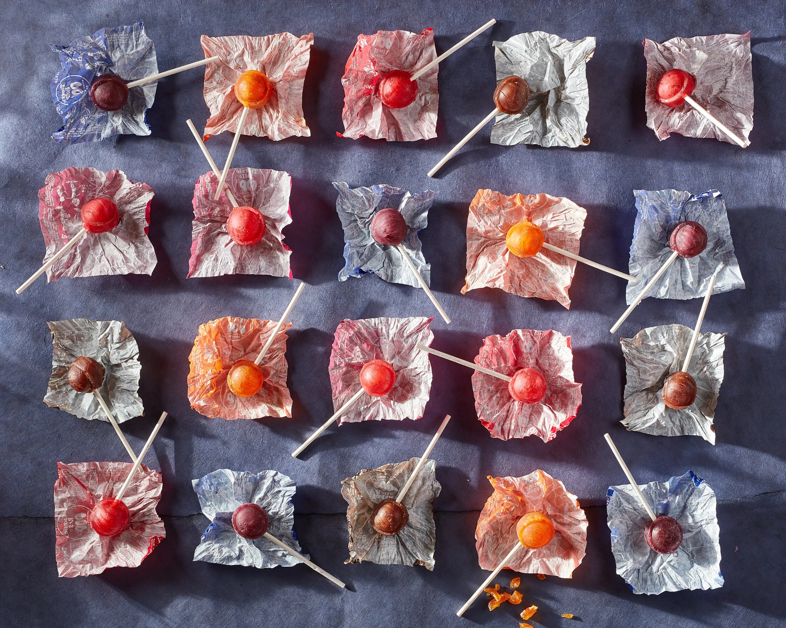 Colorful lollipops wrapped in crinkled silver, orange, and red paper arranged on a dark surface with some lollipop sticks leaning or crossing each other. Chicago Milwaukee Midwest Illinois Food Food beverage Food Drink Savory Photographers photograph