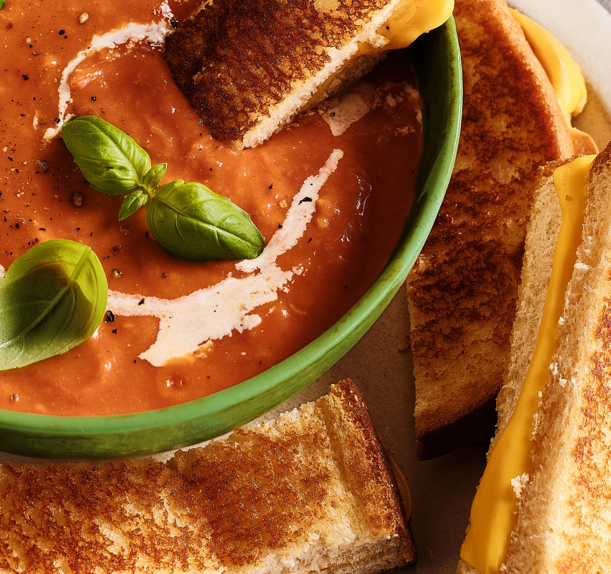 Bowl of tomato soup garnished with basil leaves, served with toasted grilled cheese sandwiches. Chicago Milwaukee Midwest Illinois Food Food beverage Food Drink Savory Photographers photographer photography videography videographer CPG Bennett Fuhrma