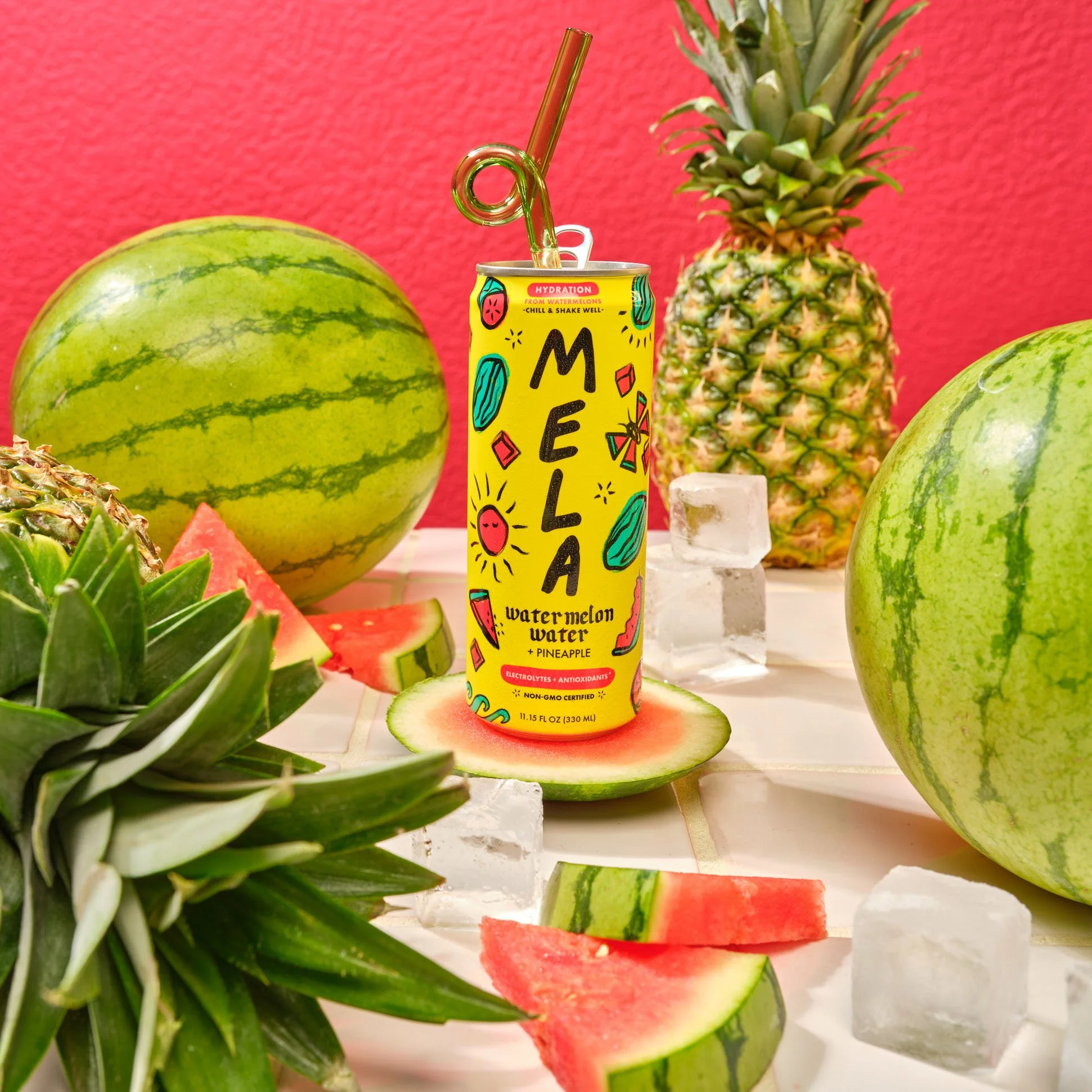 A can of Melá watermelon and pineapple flavored water surrounded by watermelons, a pineapple, an ice cube, and watermelon slices on a white surface with a pink wall background. Chicago Milwaukee Midwest Illinois Food Food beverage Food Drink Savory P
