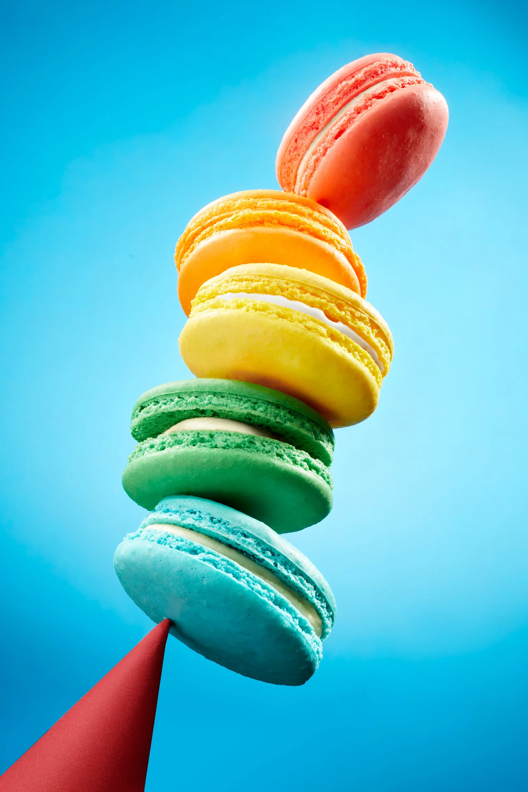 Colorful stack of six macarons in pink, orange, yellow, green, blue, and teal on a blue background. Chicago Milwaukee Midwest Illinois Food Food beverage Food Drink Savory Photographers photographer photography videography videographer CPG Bennett Fu