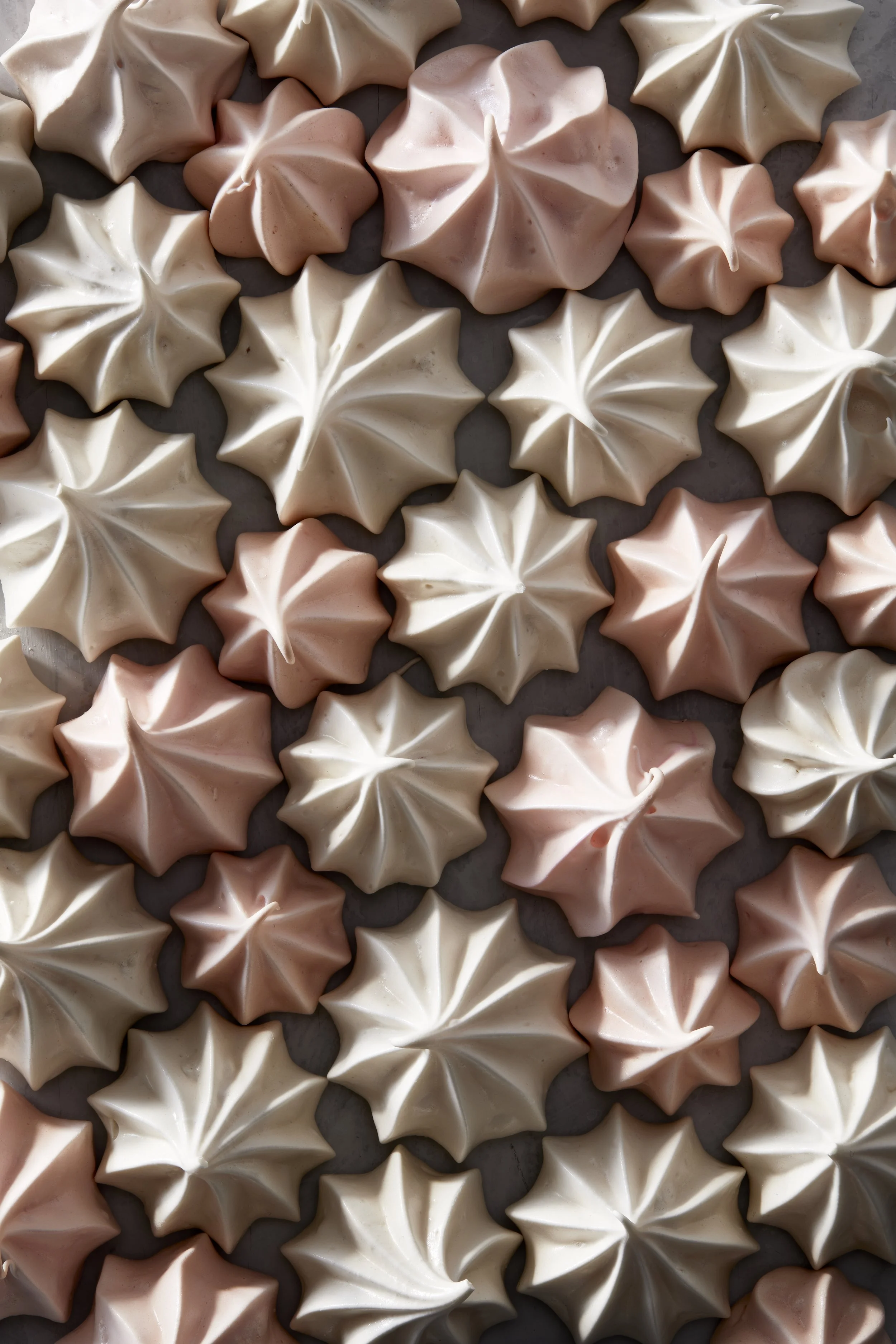 A close-up of assorted meringue cookies in white, light pink, and beige colors, arranged on a baking sheet. Chicago Milwaukee Midwest Illinois Food Food beverage Food Drink Savory Photographers photographer photography videography videographer CPG Be