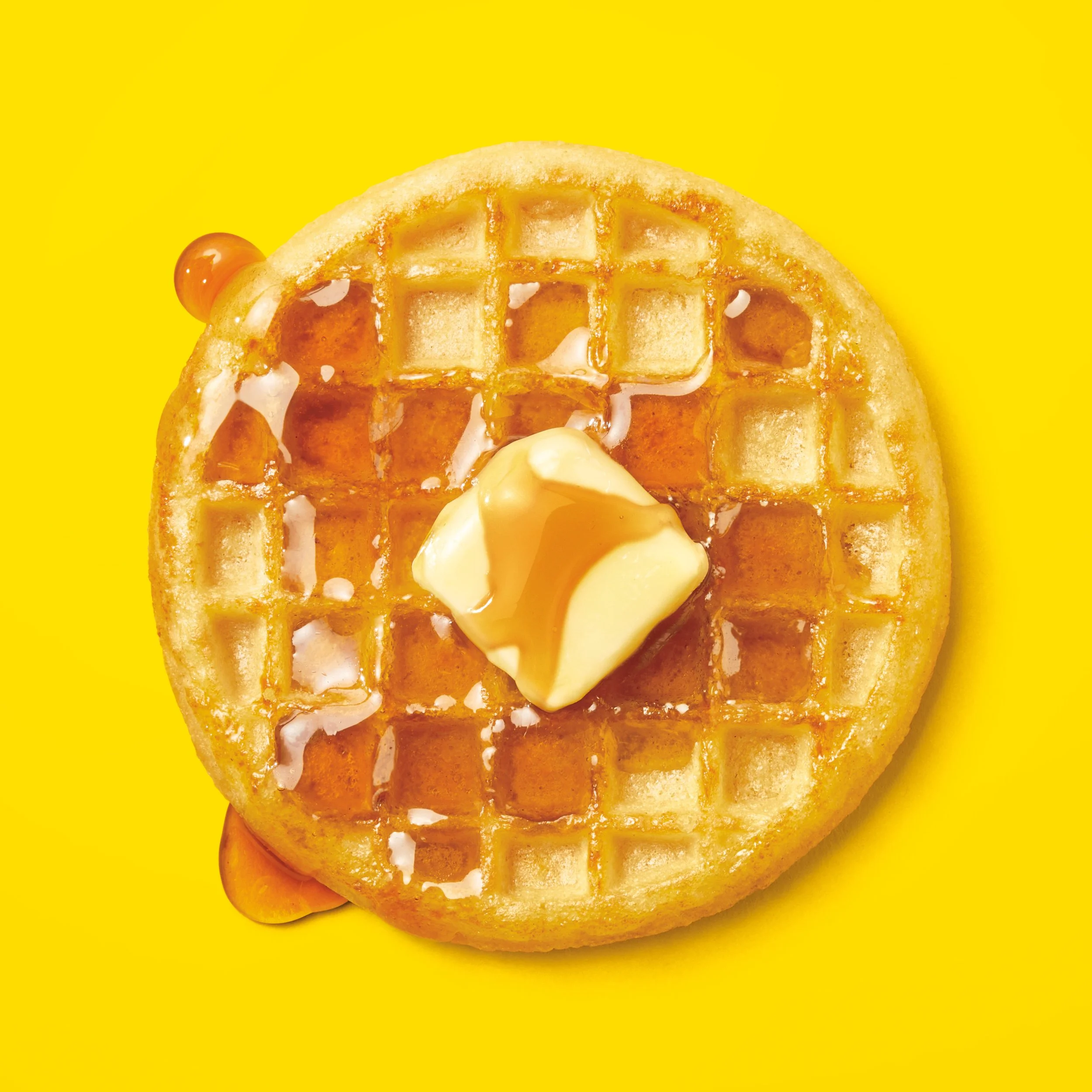 A round waffle with a pat of butter and syrup on top, placed on a bright yellow background. Chicago Milwaukee Midwest Illinois Food Food beverage Food Drink Savory Photographers photographer photography videography videographer CPG Bennett Fuhrman Be