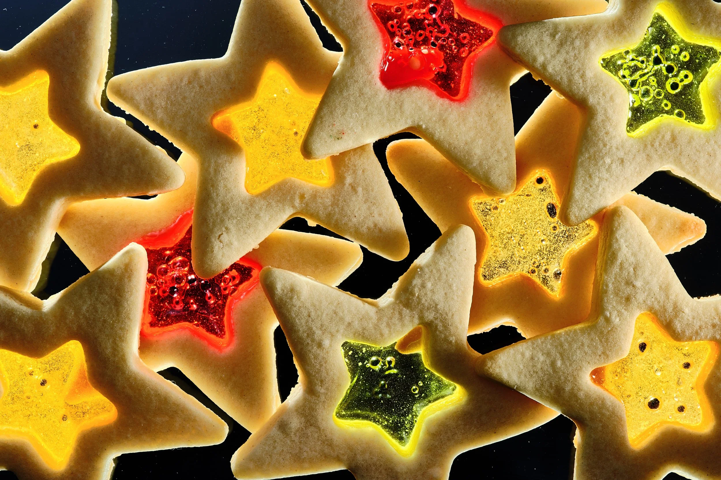Star-shaped cookies with colorful, glowing jelly centers in red, yellow, and green, placed on a black background. Chicago Milwaukee Midwest Illinois Food Food beverage Food Drink Savory Photographers photographer photography videography videographer 