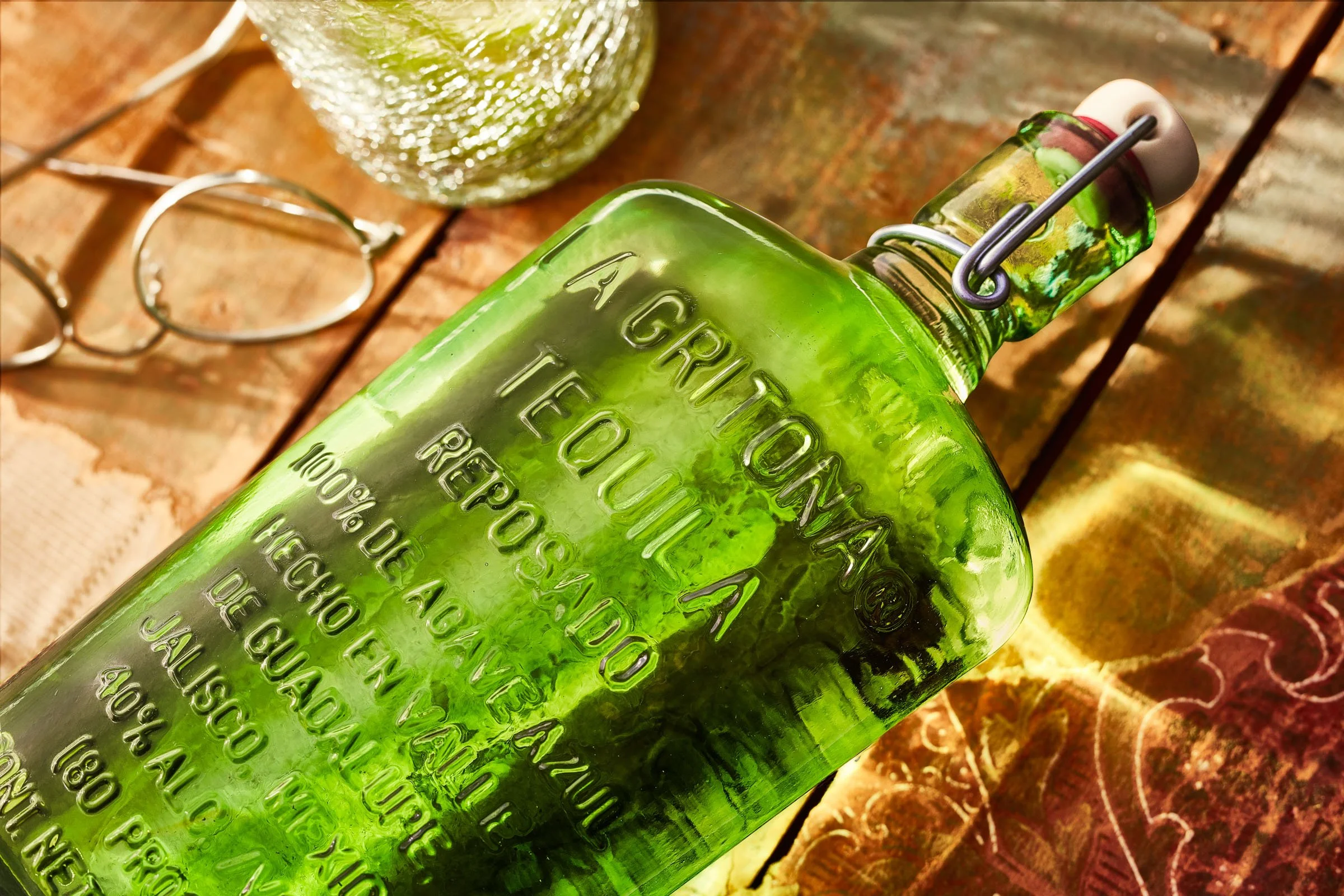 Close-up of a green glass bottle with embossed text, placed on a wooden surface, with some accessories like earrings and a textured glass object nearby. Chicago Milwaukee Midwest Illinois Food Food beverage Food Drink Savory Photographers photographe