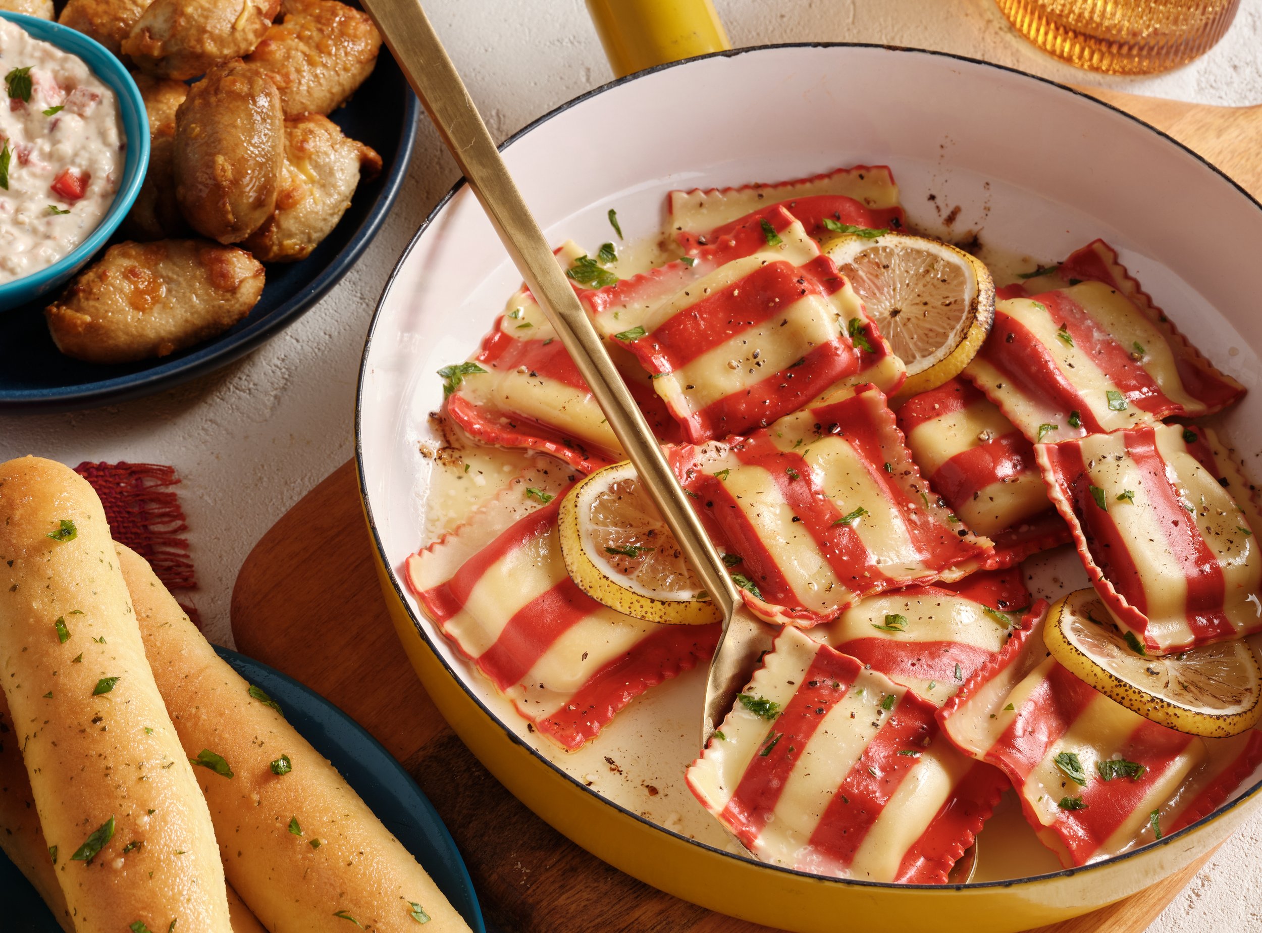 A dish of striped pasta with red and white sauce, garnished with lemon slices and chopped herbs, with side dishes of breadsticks, chicken wings, and a creamy dip or salad. Chicago Milwaukee Midwest Illinois Food Food beverage Food Drink Savory Photog