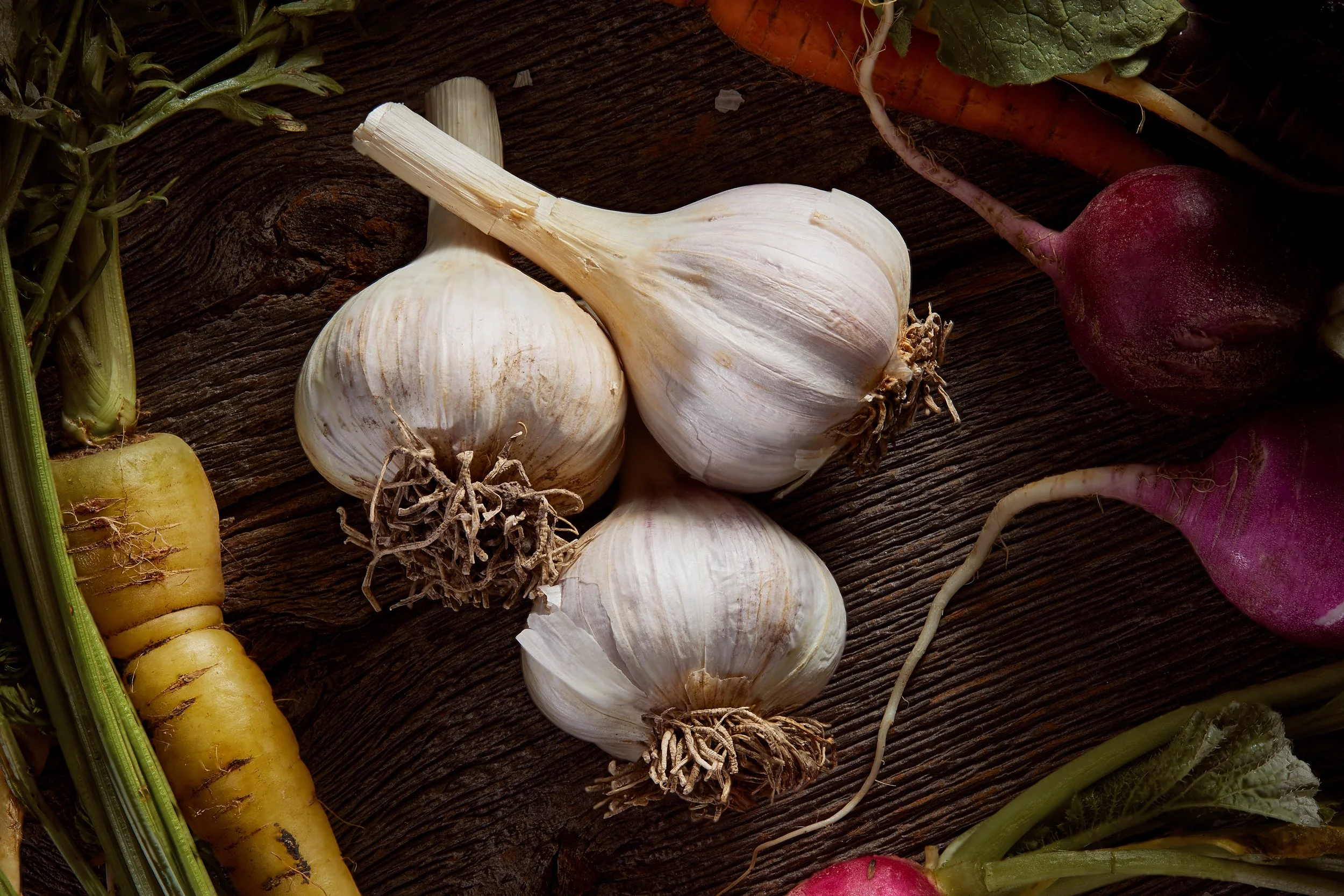 Fresh garlic bulbs, carrots, and radishes on a wooden surface. Chicago Milwaukee Midwest Illinois Food Food beverage Food Drink Savory Photographers photographer photography videography videographer CPG Bennett Fuhrman Ben Tiny Scheme