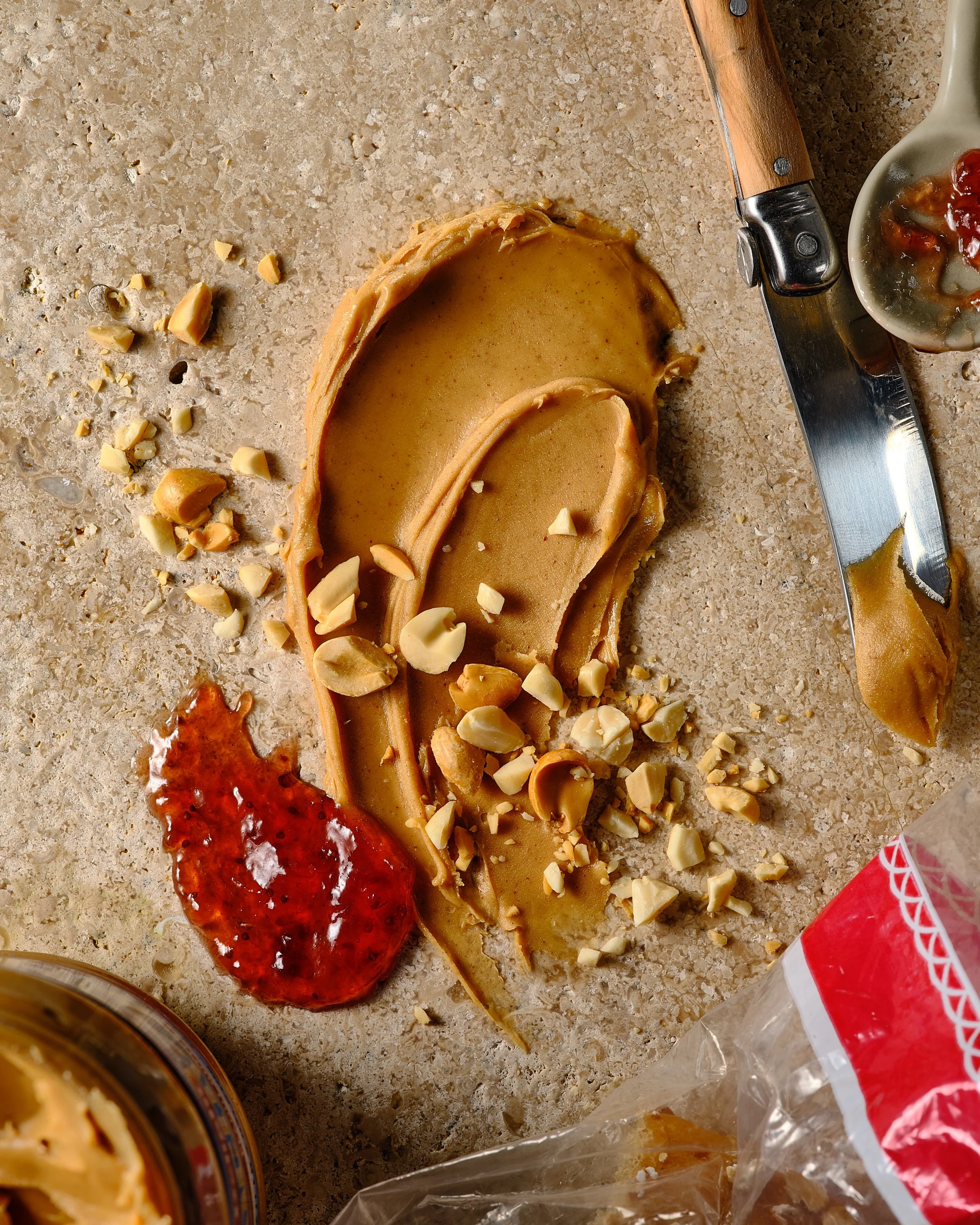 Peanut butter cookies with chopped nuts on a kitchen countertop, with a knife and a spoon of jam nearby. Chicago Milwaukee Midwest Illinois Food Food beverage Food Drink Savory Photographers photographer photography videography videographer CPG Benne