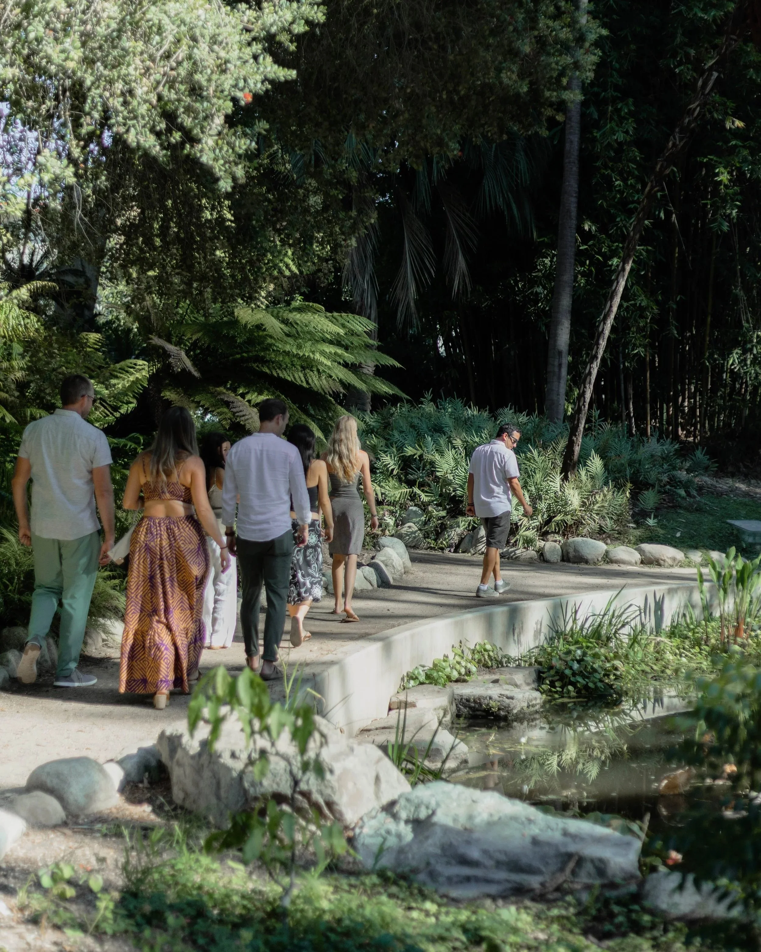 Group of people walking on a pathway in a lush garden with trees and plants.