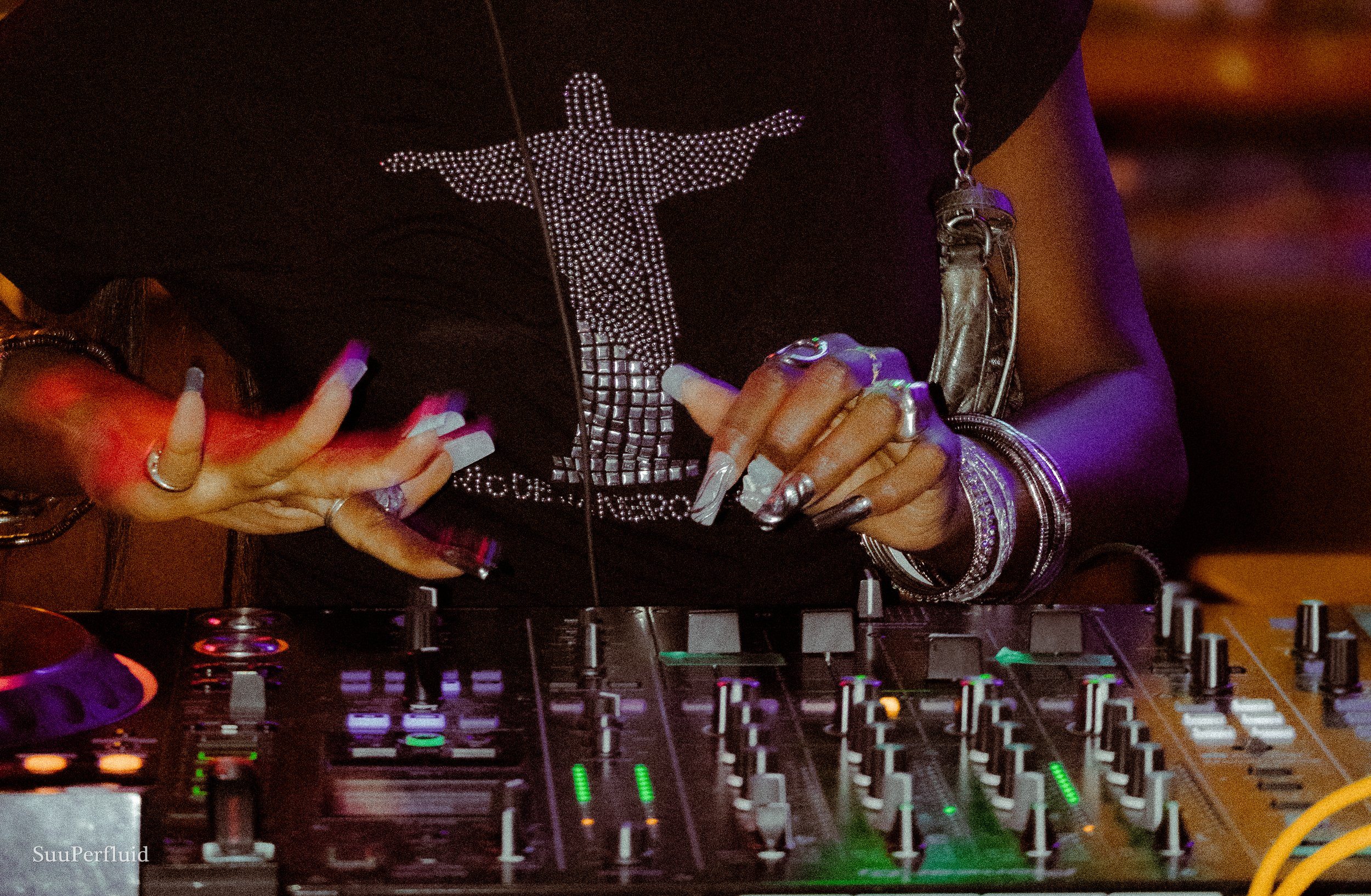 Visuel d'un.e DJ portant un tee-shirt strassé "Rio de Janeiro", avec de longs ongles, qui manipule sa platine
