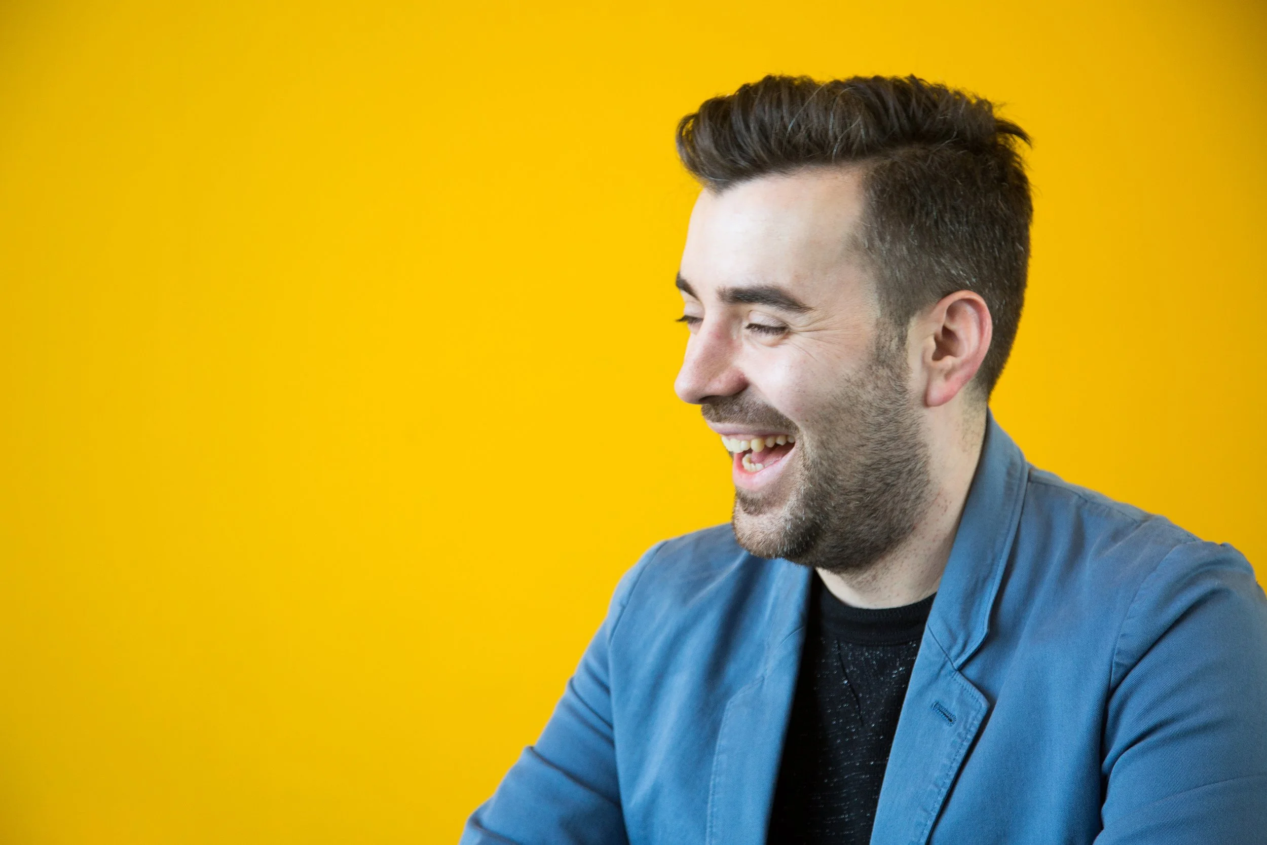 Man smiling in blue jacket against a yellow background