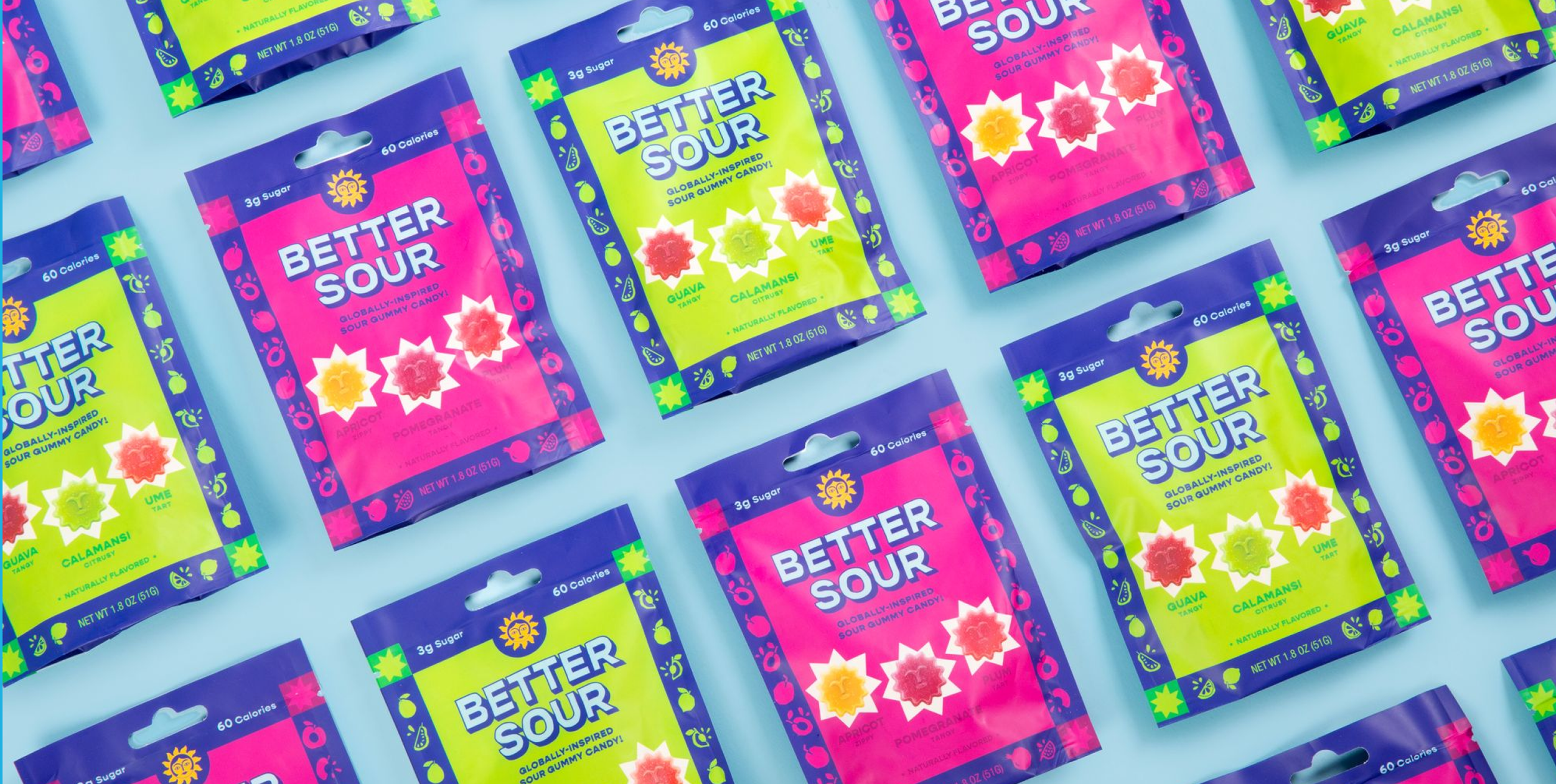 Multiple colorful packages of sour gummy candy on a light blue background. The packages are pink and green with blue borders, labeled "Better Sour" and feature fruit illustrations including apricot, pomegranate, guava, and calamansi.