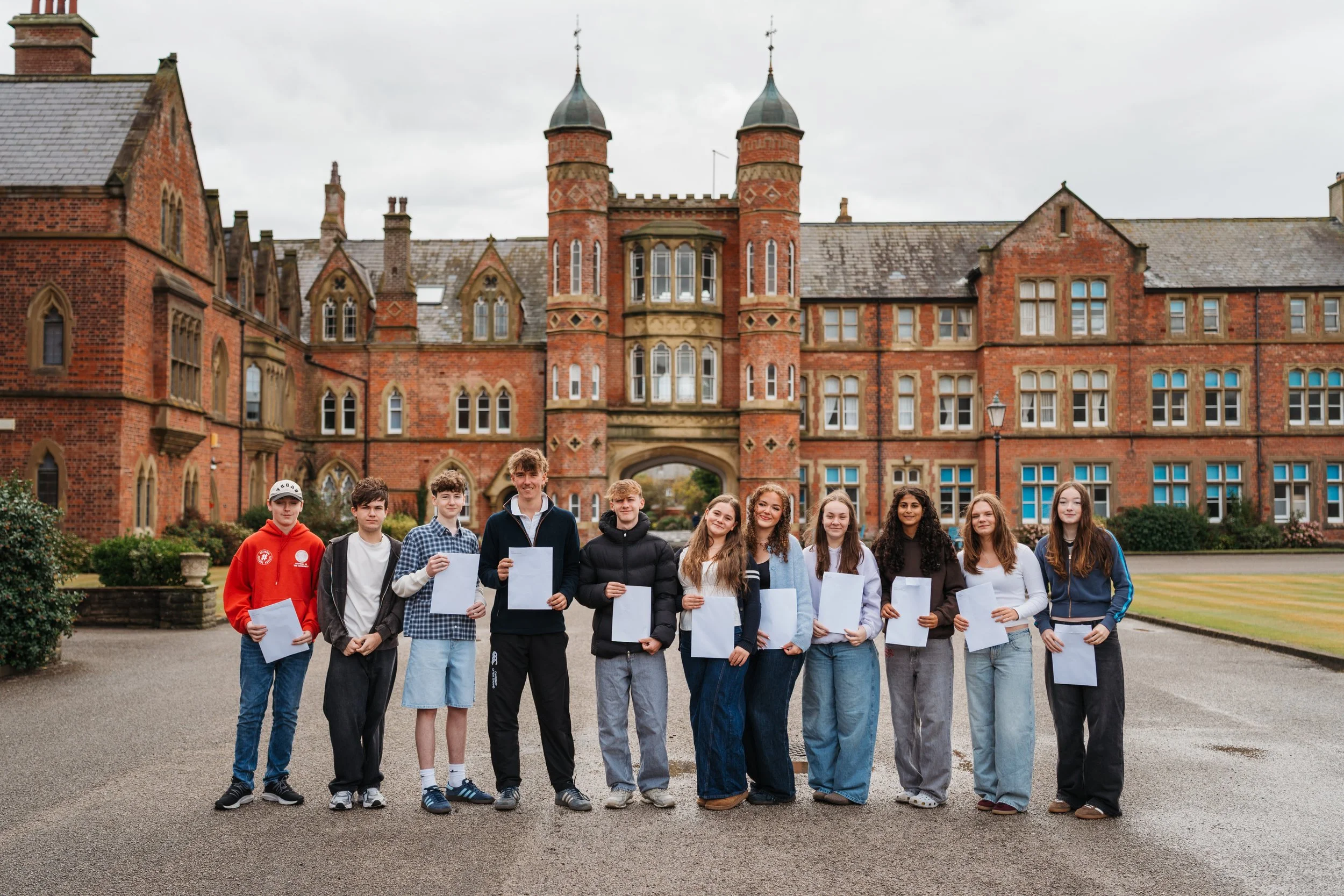 11 Rossall students pose with their GCSE results in front of the Archway
