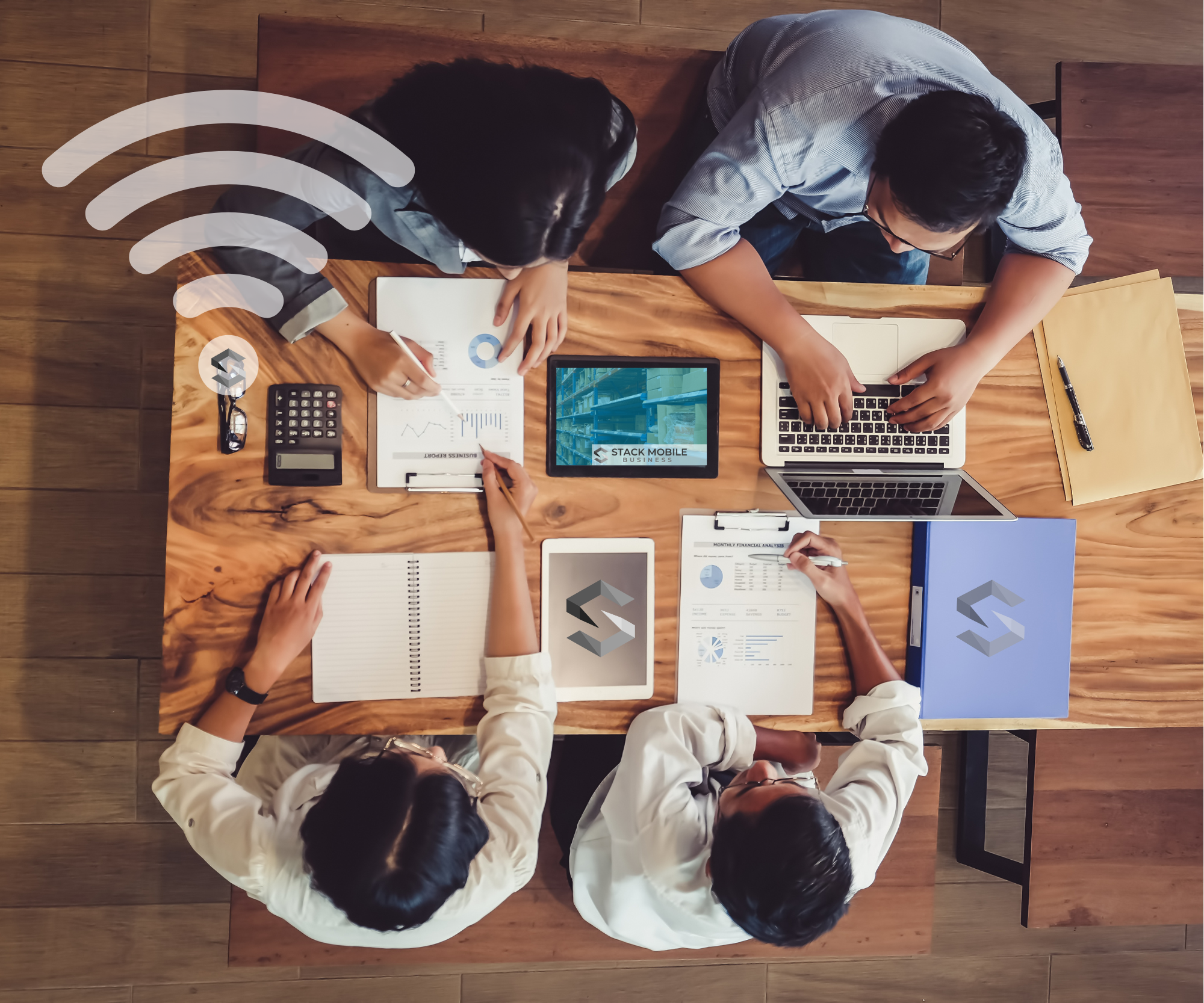 A top-down view of four people working together at a wooden table, with laptops, tablets, notebooks, and documents displaying charts and graphs. There is a Wi-Fi symbol overlayed on the image.