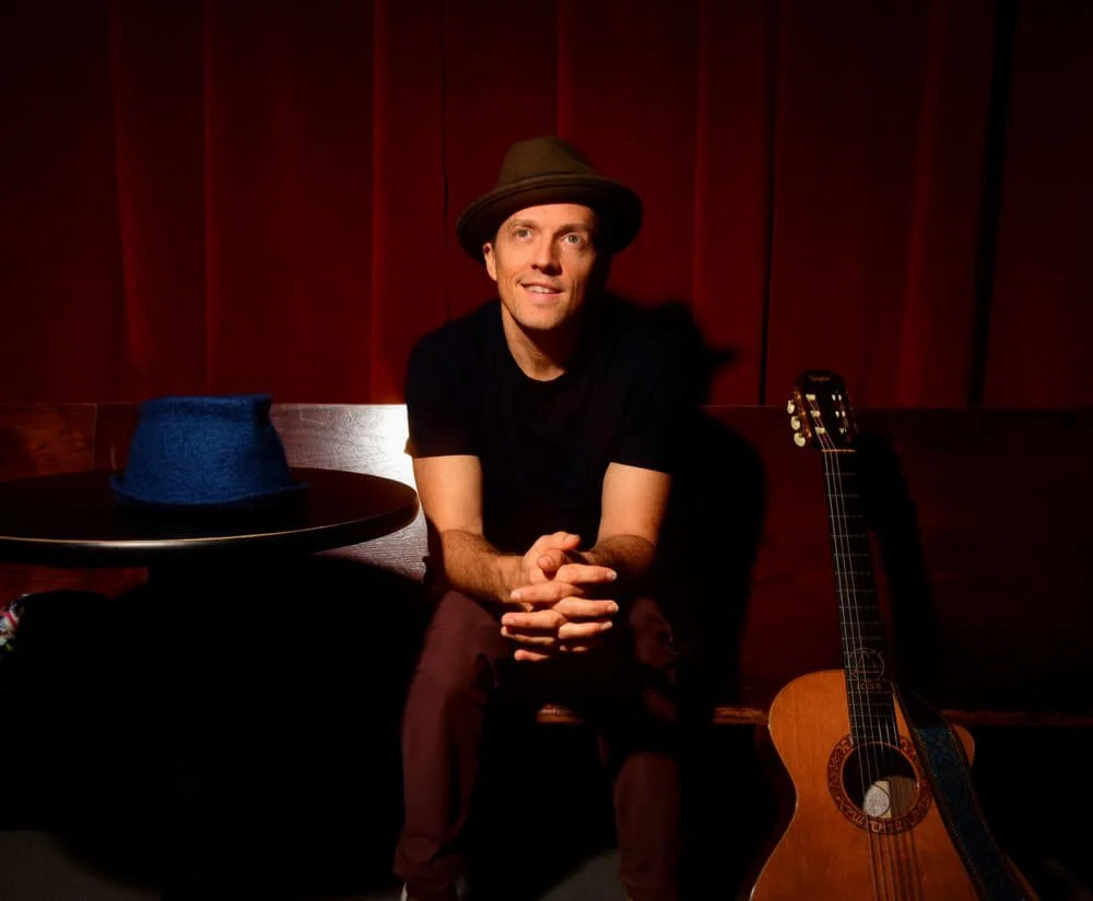 Jason Mraz sitting down beside a guitar