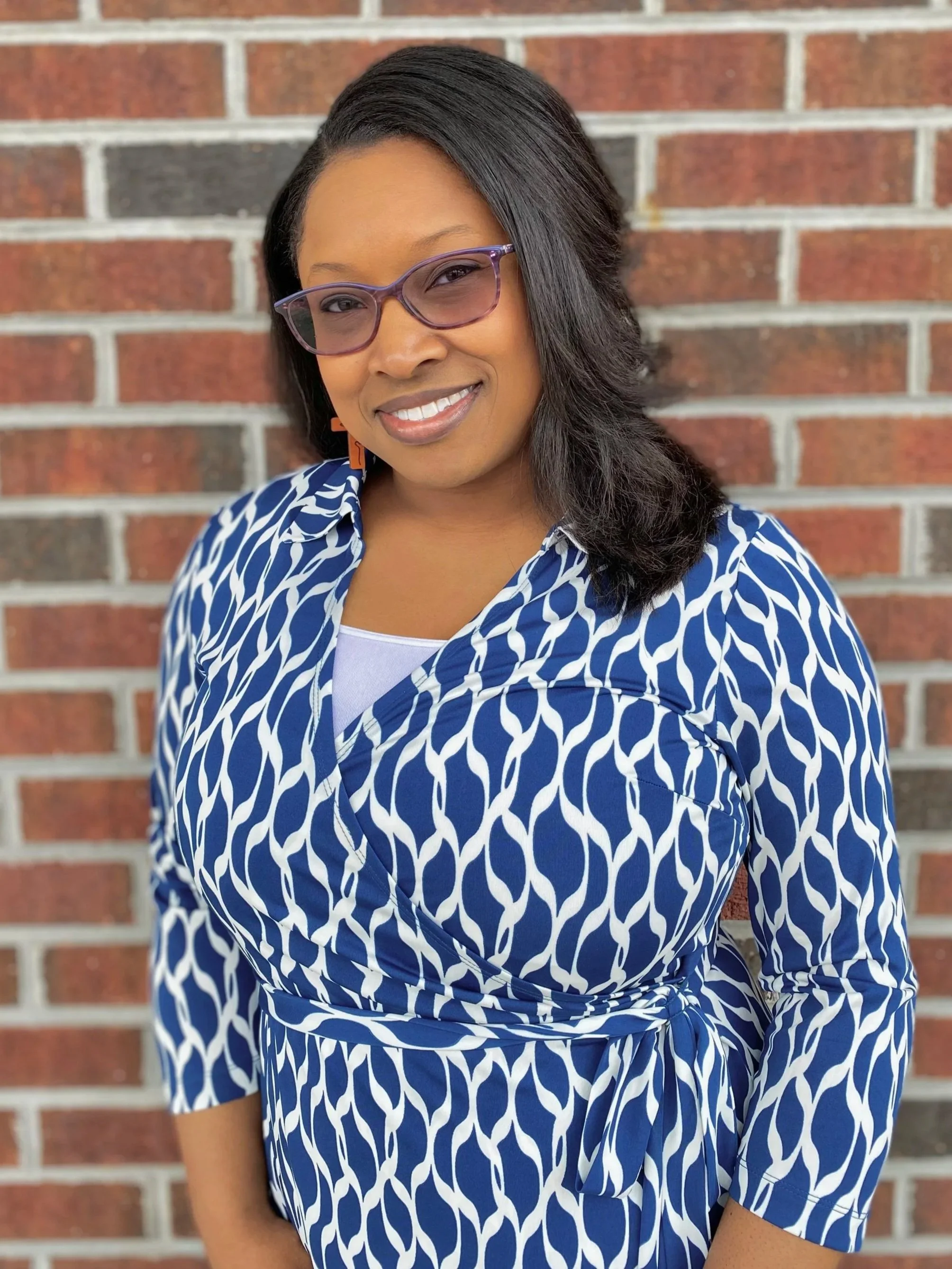 Woman in sunglasses and a beige dress standing on a beach with the ocean in the background.