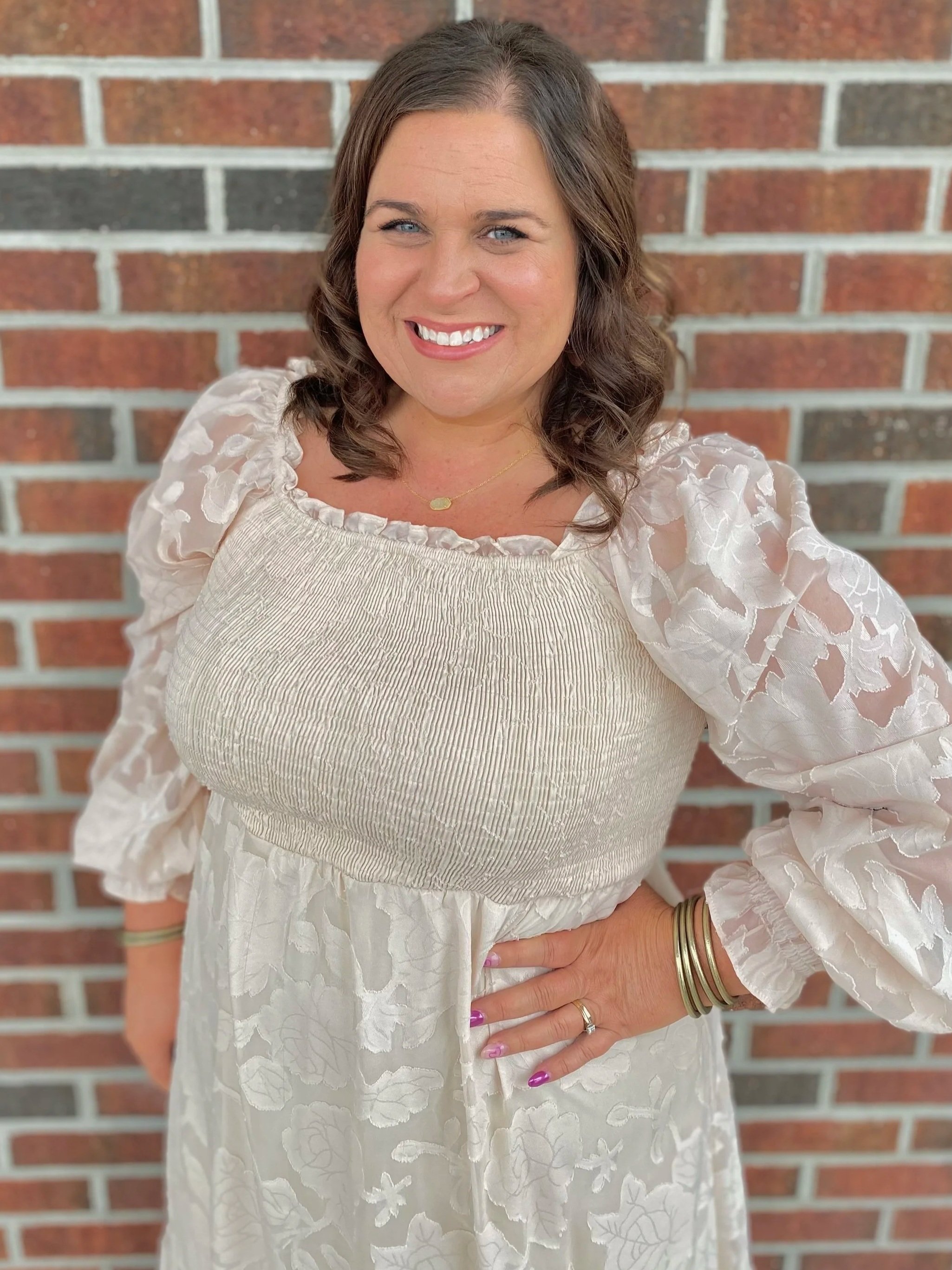 Woman smiling in a light blue dress against a shiplap wall.