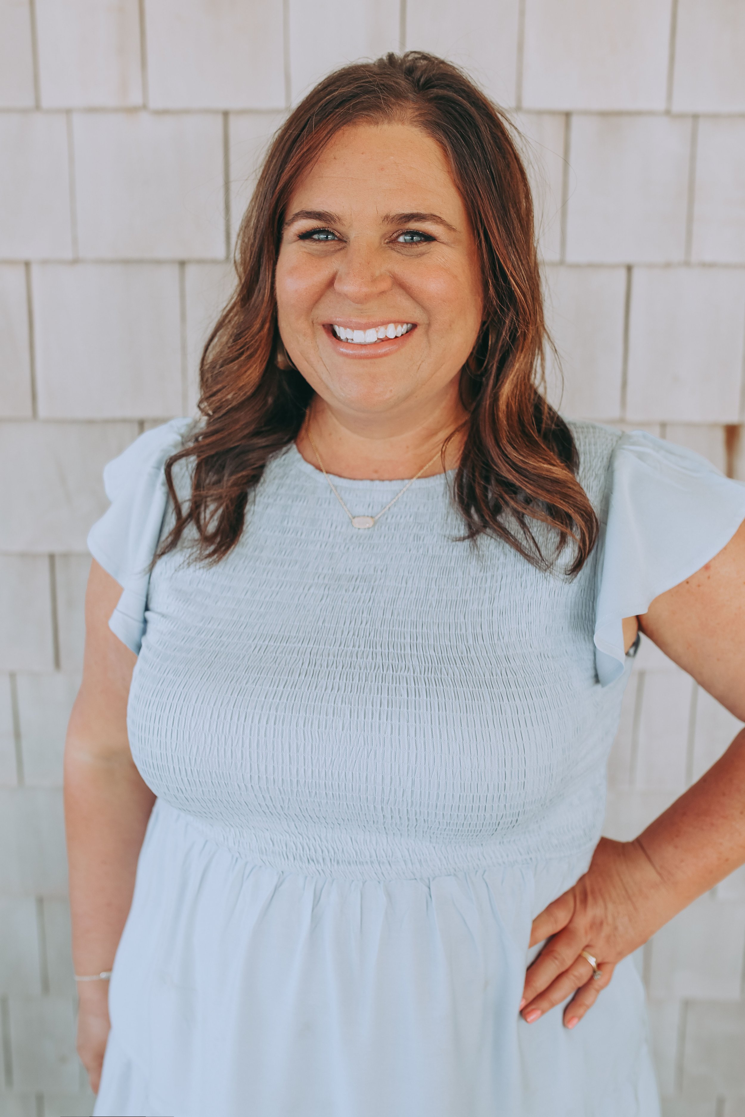 Woman smiling in a light blue dress against a shiplap wall.