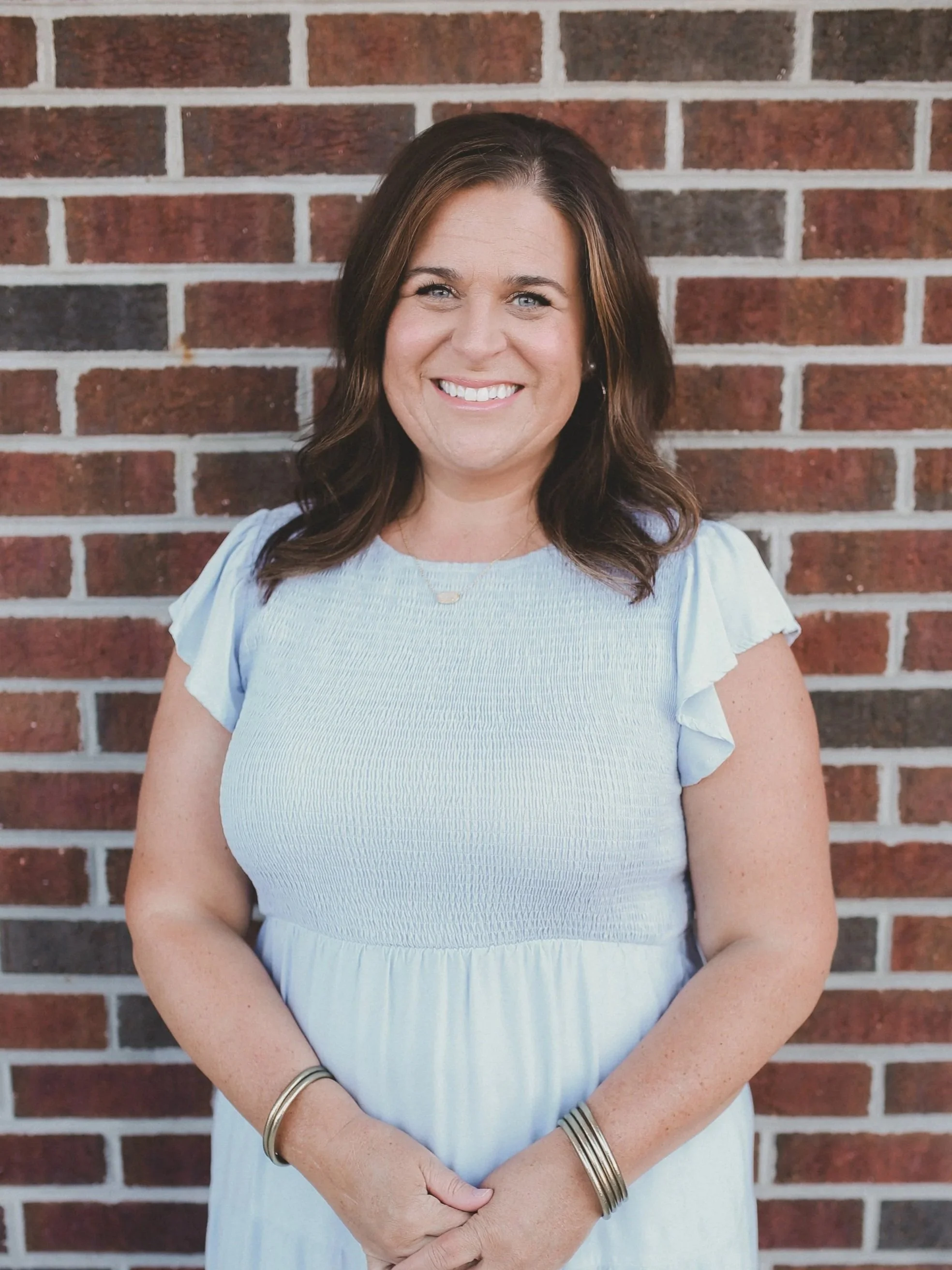 Woman smiling in a light blue dress against a shiplap wall.