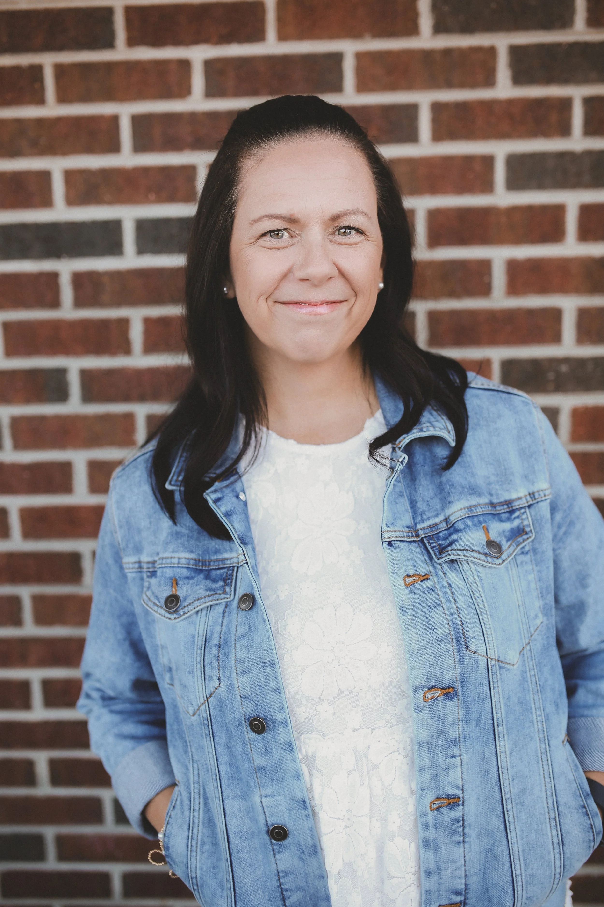 Woman wearing a jean jacket and white dress standing in front of a shingle wall