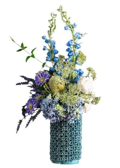 A tall blue ceramic vase holding a mixed arrangement of flowers including purple, white, and blue blooms with green foliage.