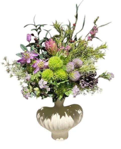 Arrangement of various purple and green flowers and foliage in a white ceramic vase.