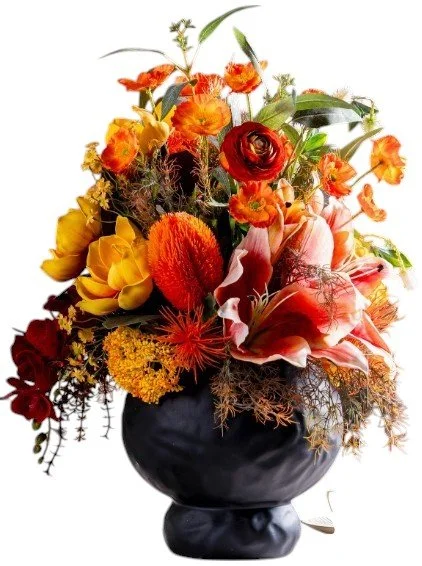 Vase with a vibrant arrangement of orange, yellow, and red flowers and green foliage.