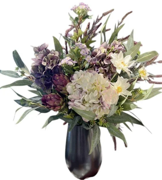 A bouquet of mixed flowers including hydrangeas, artichokes, and lilies in a dark vase.