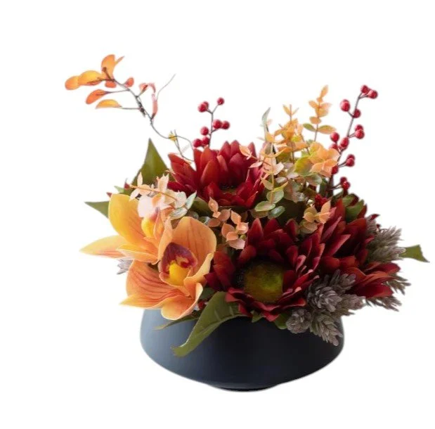 Artificial floral arrangement in a black vase with orange orchids, red and burgundy flowers, green foliage, and small red berries.