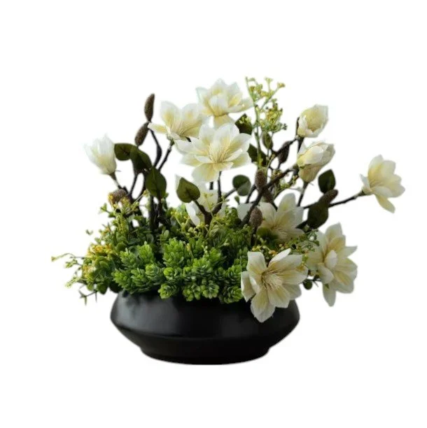 Artificial floral arrangement with white flowers and green foliage in a black ceramic bowl