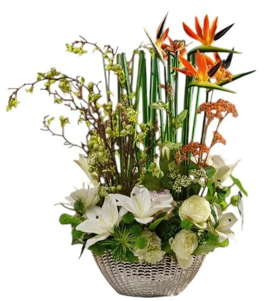 Arrangement of tropical flowers including white lilies, calla lilies, orange Bird of Paradise, and other greenery in a decorative silver bowl