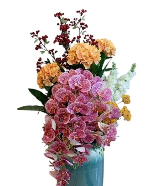 Colorful floral arrangement in a turquoise vase, including pink orchids, orange hydrangeas, white snapdragons, and red berries.