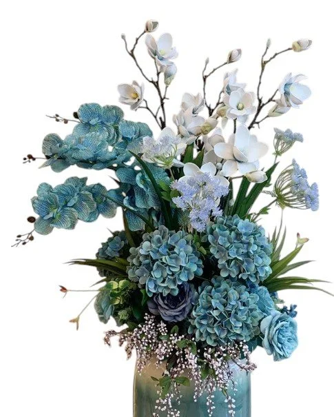 Blue and white artificial flower arrangement in a glass vase, featuring hydrangeas, orchids, roses, and other small flowers.