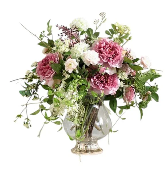 A bouquet of pink and white flowers, including carnations and other blossoms, arranged with green leaves in a clear glass vase.