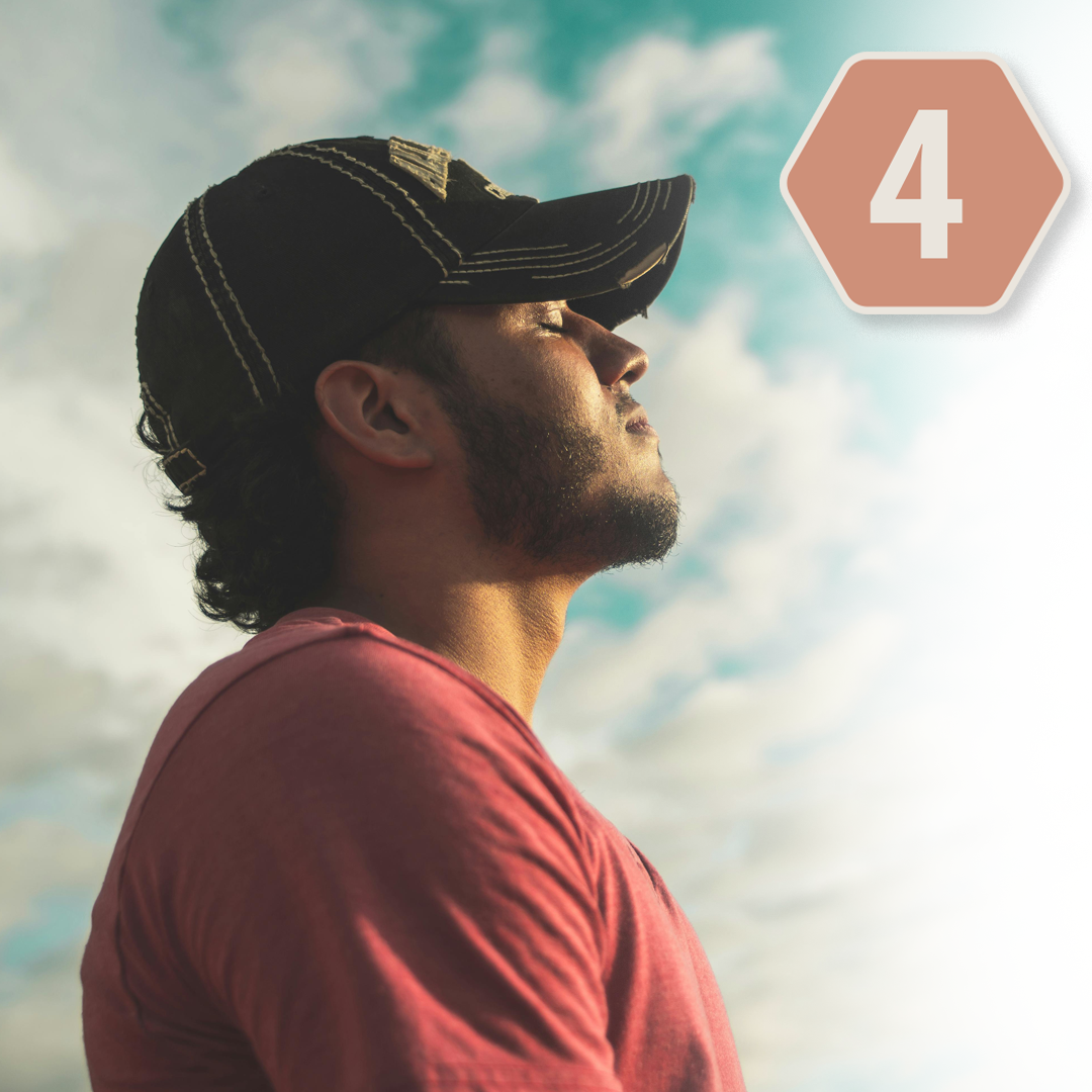 A man wearing a baseball cap and a red shirt looking up outdoors with a cloudy sky in the background.