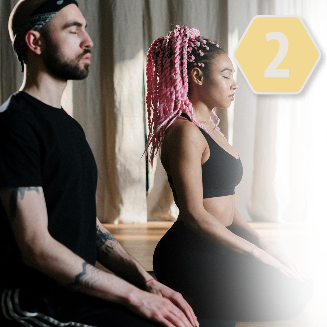 Man and woman meditating in a yoga class, sitting cross-legged with eyes closed.