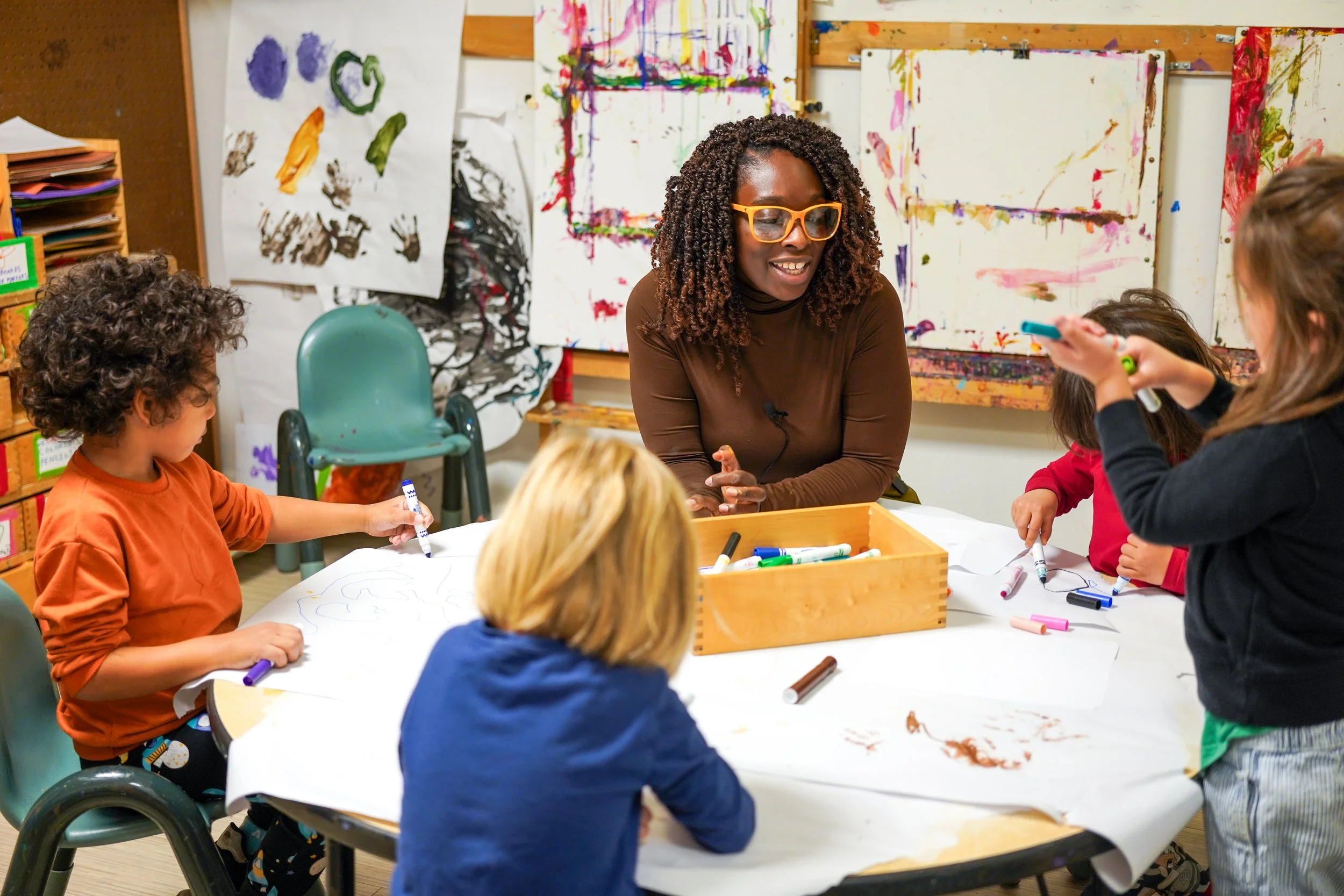 Peggy Francois at a classroom table with Maple Street Students who are coloring with markers.